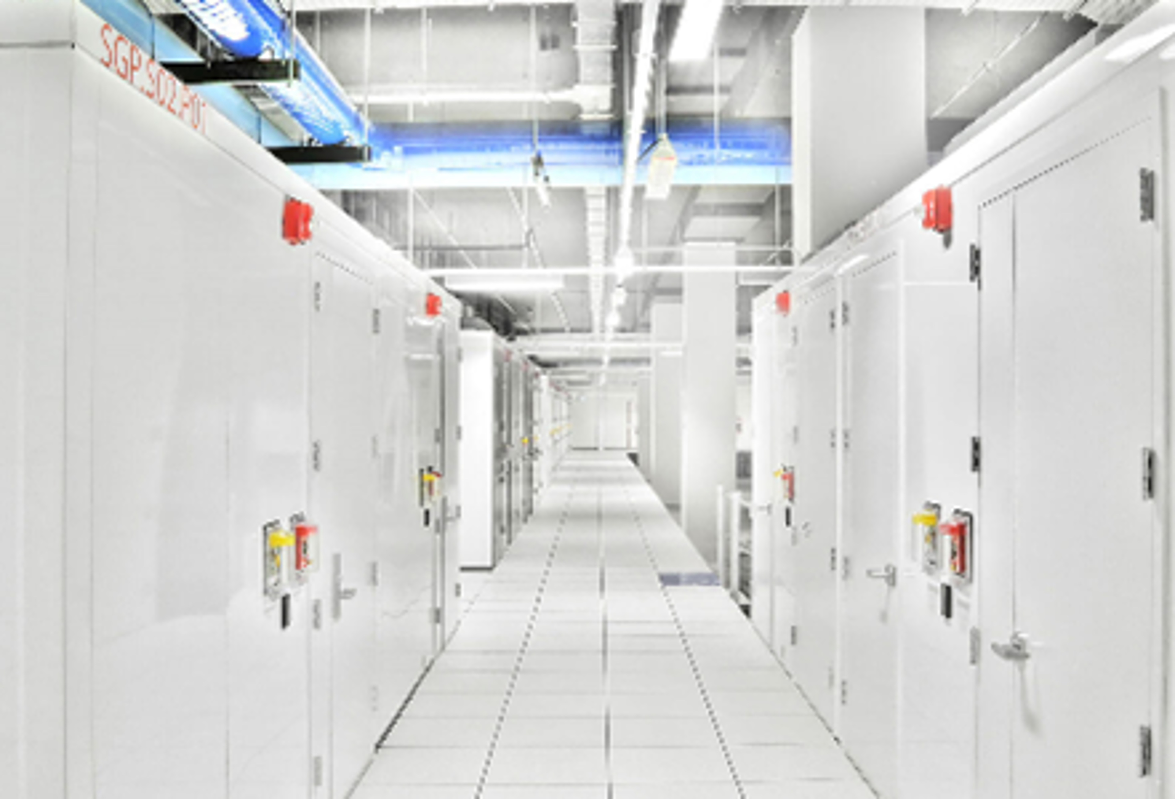 A brightly lit corridor in a data center fitout in Singapore, featuring rows of white server cabinets and overhead piping systems.