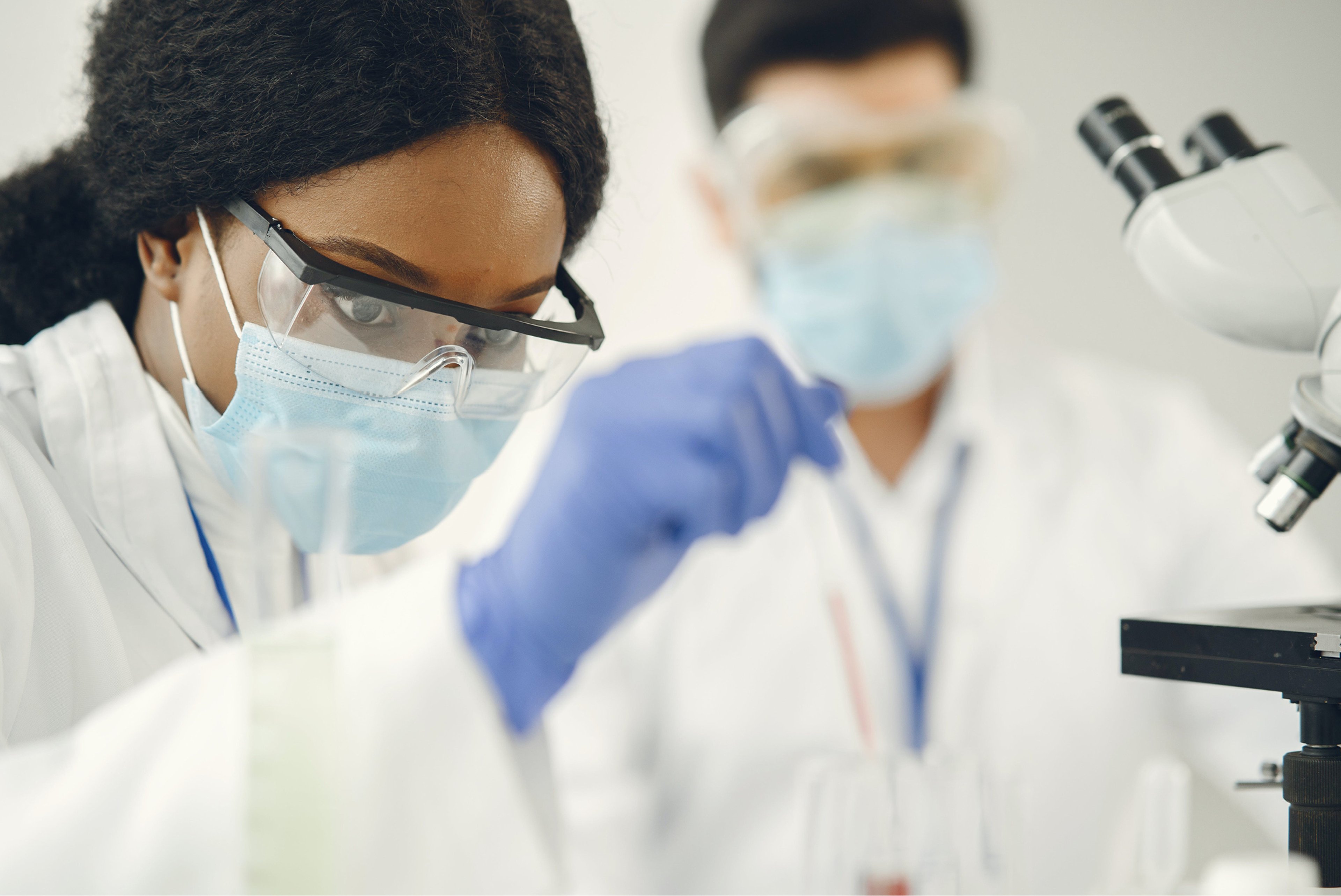 Female scientist with glasses, face mask and gloves in front of lab equipment and a microscope