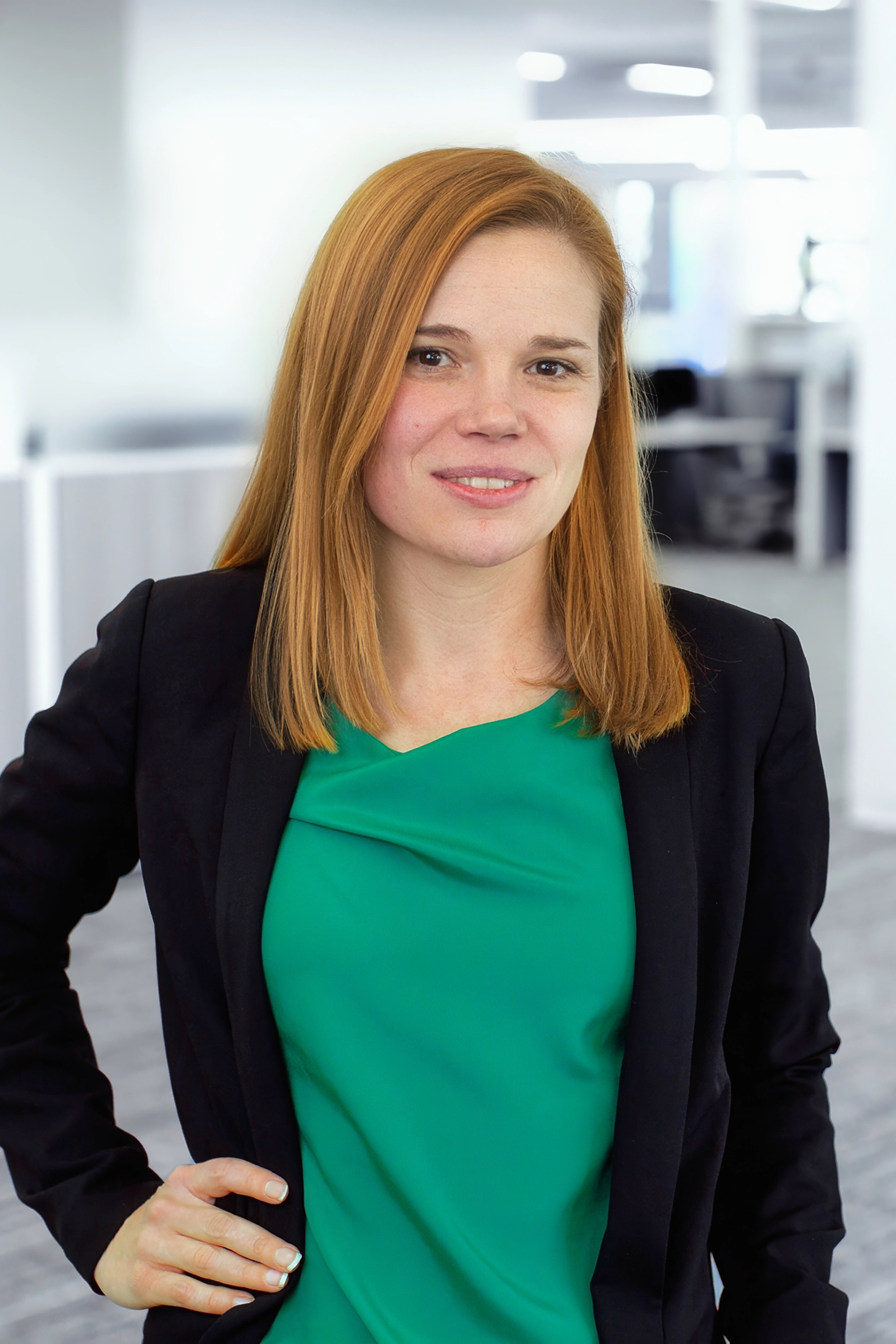 Chelsea Miller is seen wearing a green top and black blazer, standing confidently with a slight smile in a professional office setting.