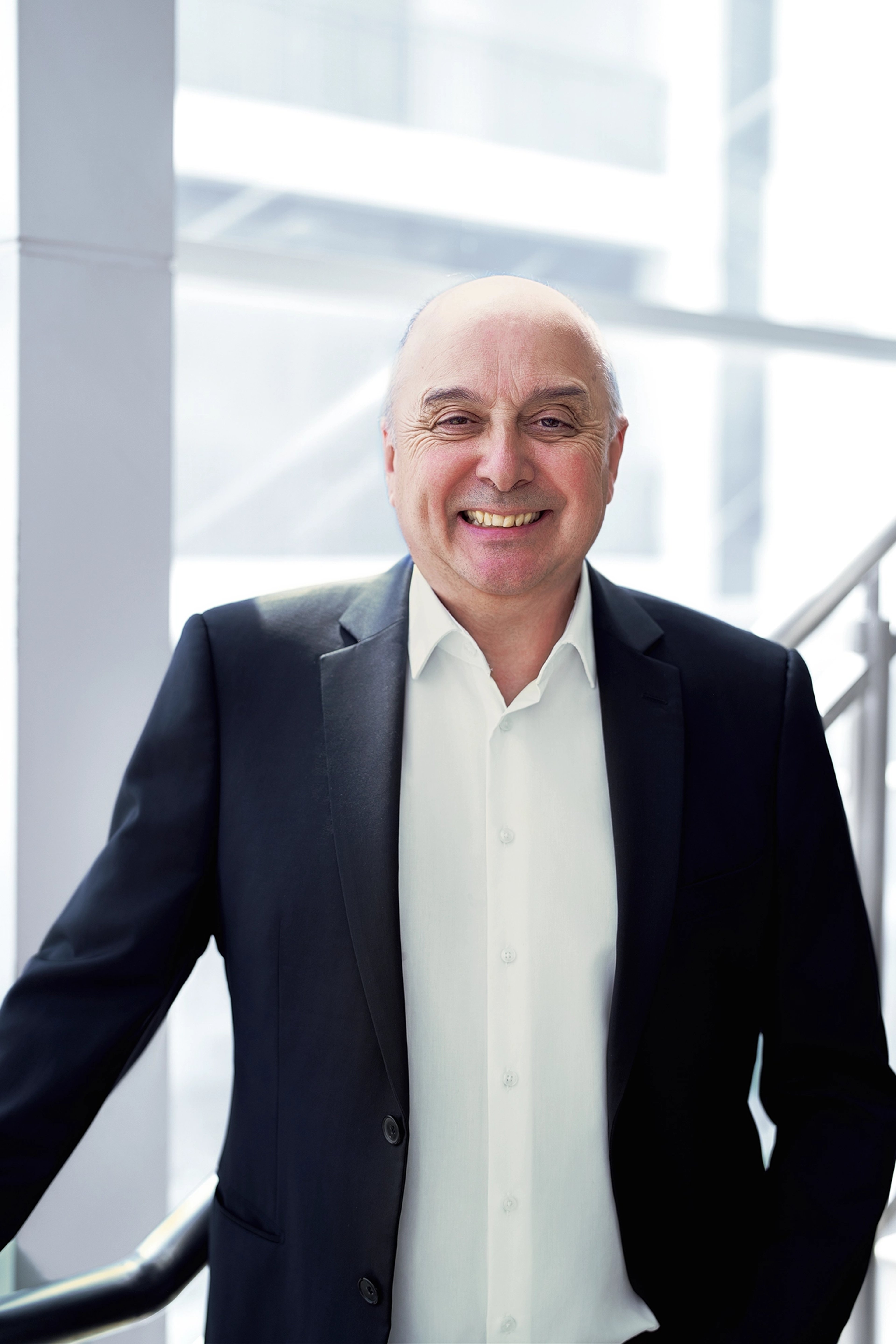 Gavin Francis standing in a well-lit environment, wearing a dark suit jacket over a white shirt, smiling at the camera.