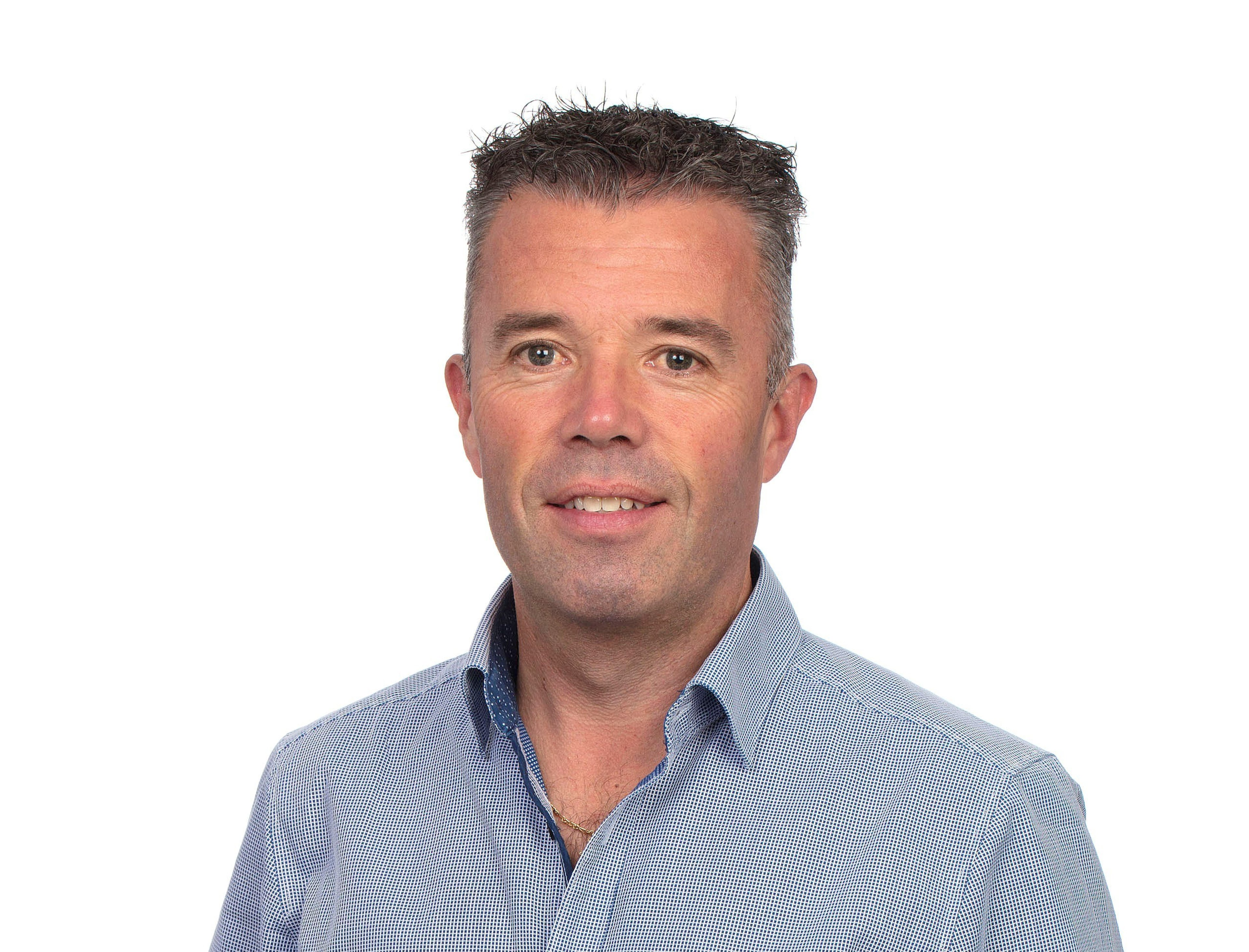 Padraig Finn is pictured wearing a light blue button-up shirt, smiling in front of a plain white background.