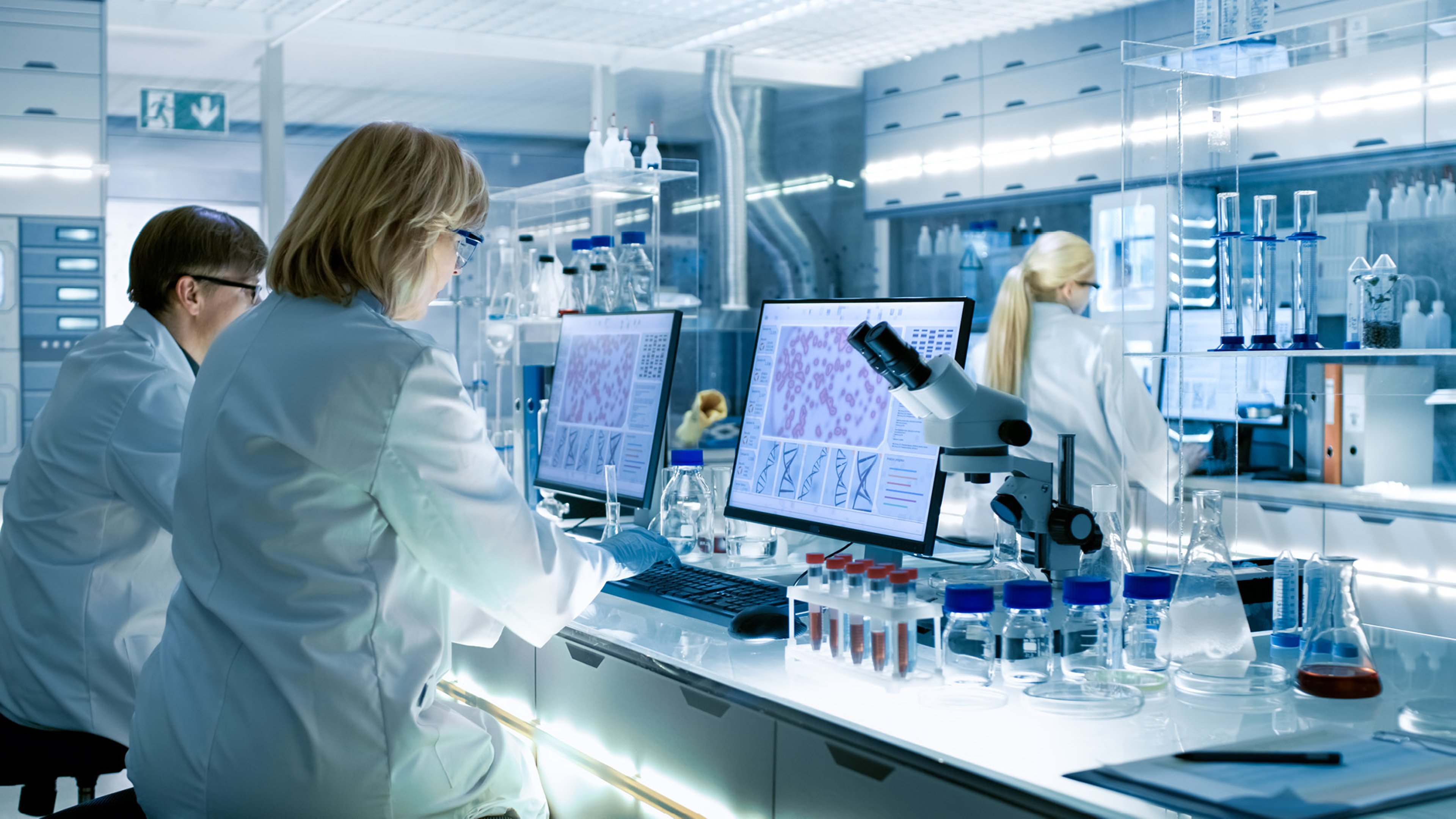 Scientists working in a modern lab, analyzing data on computer screens surrounded by lab equipment.
