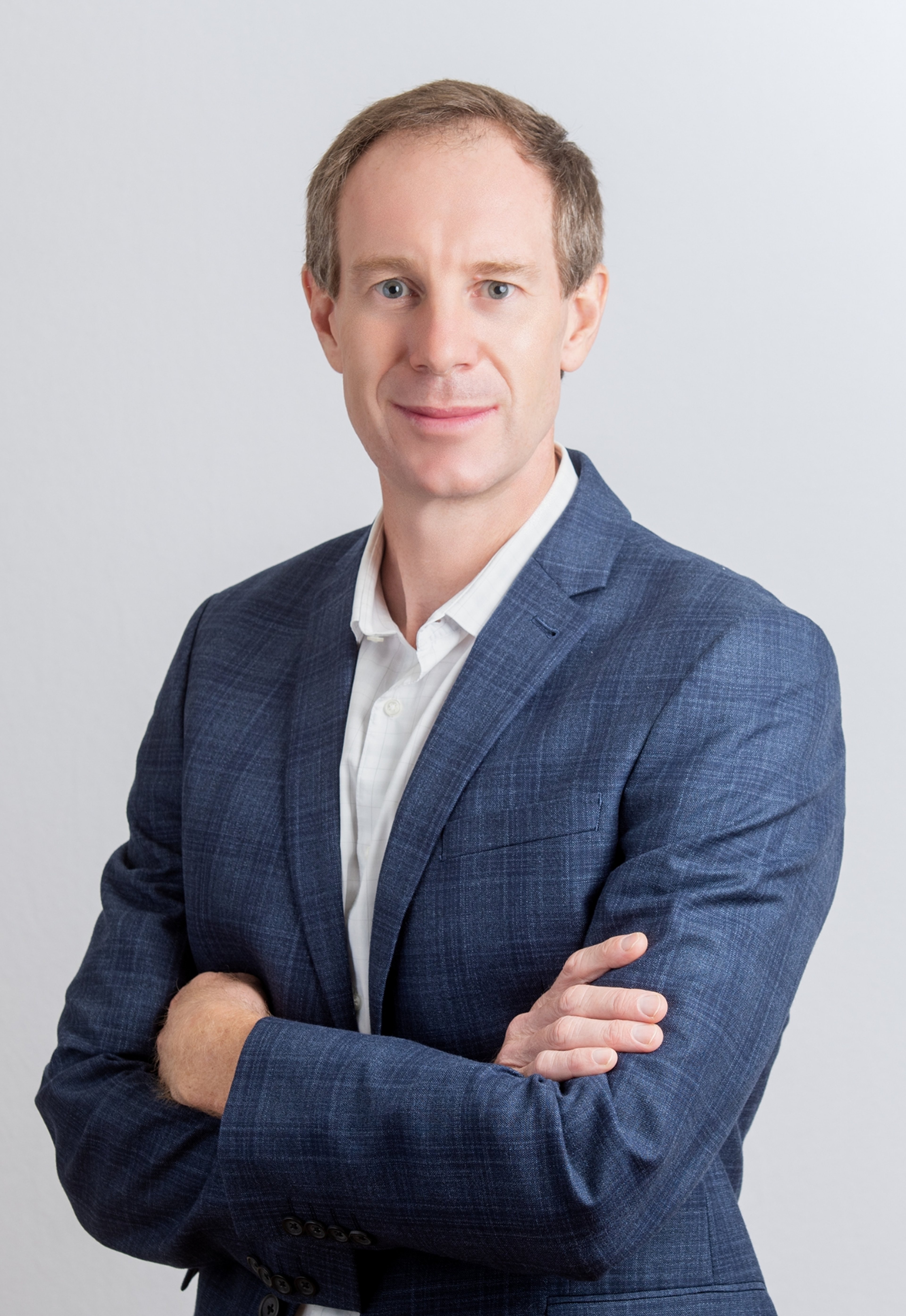 A portrait of Anthony Brown, who is standing with his arms crossed. He is wearing a blue suit jacket over a white shirt, looking directly at the camera with a calm expression.