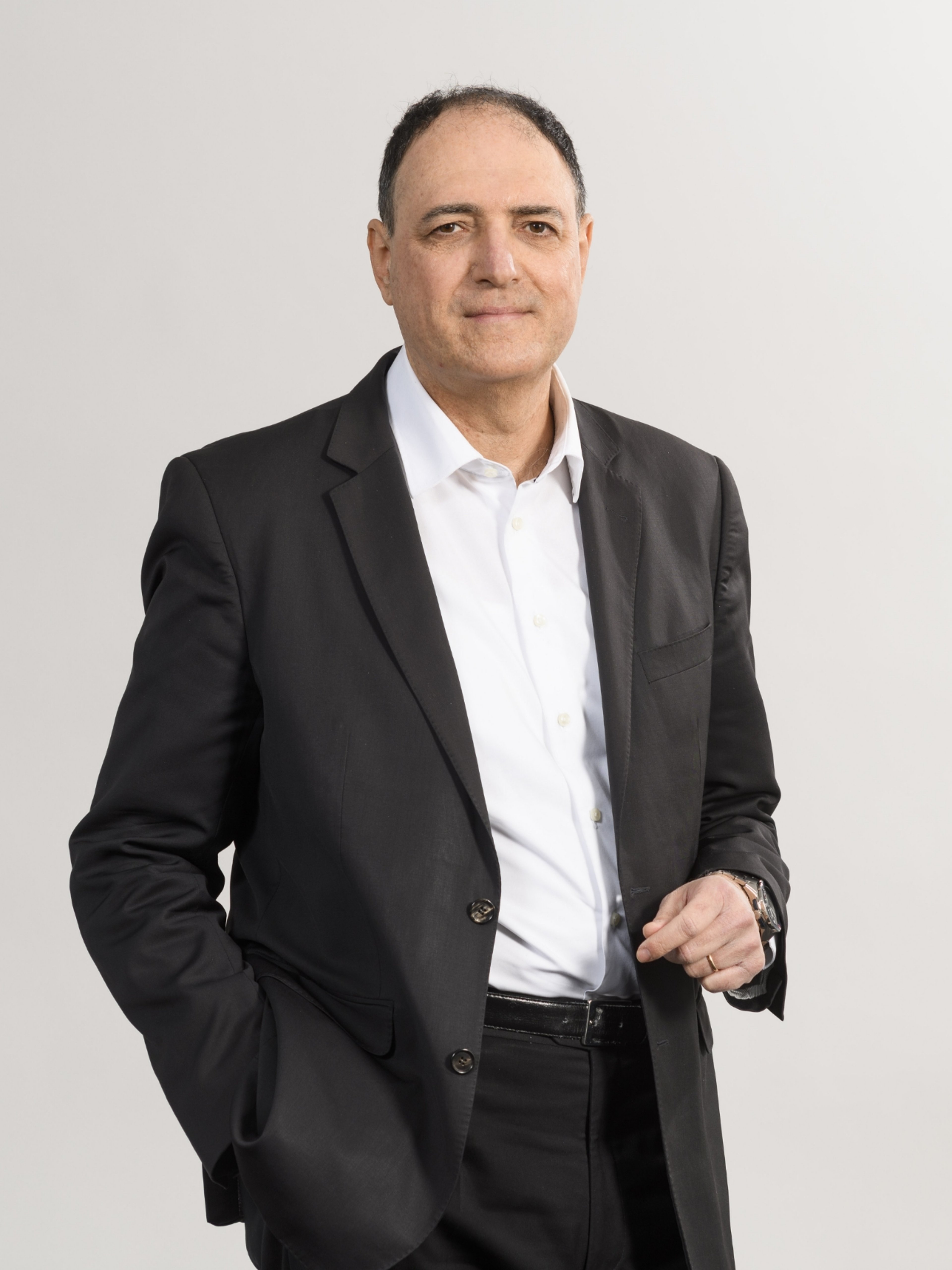 Luca Mussati, dressed in a black suit with a white shirt, standing confidently with one hand in his pocket and the other resting at his side. He has a calm expression on his face.