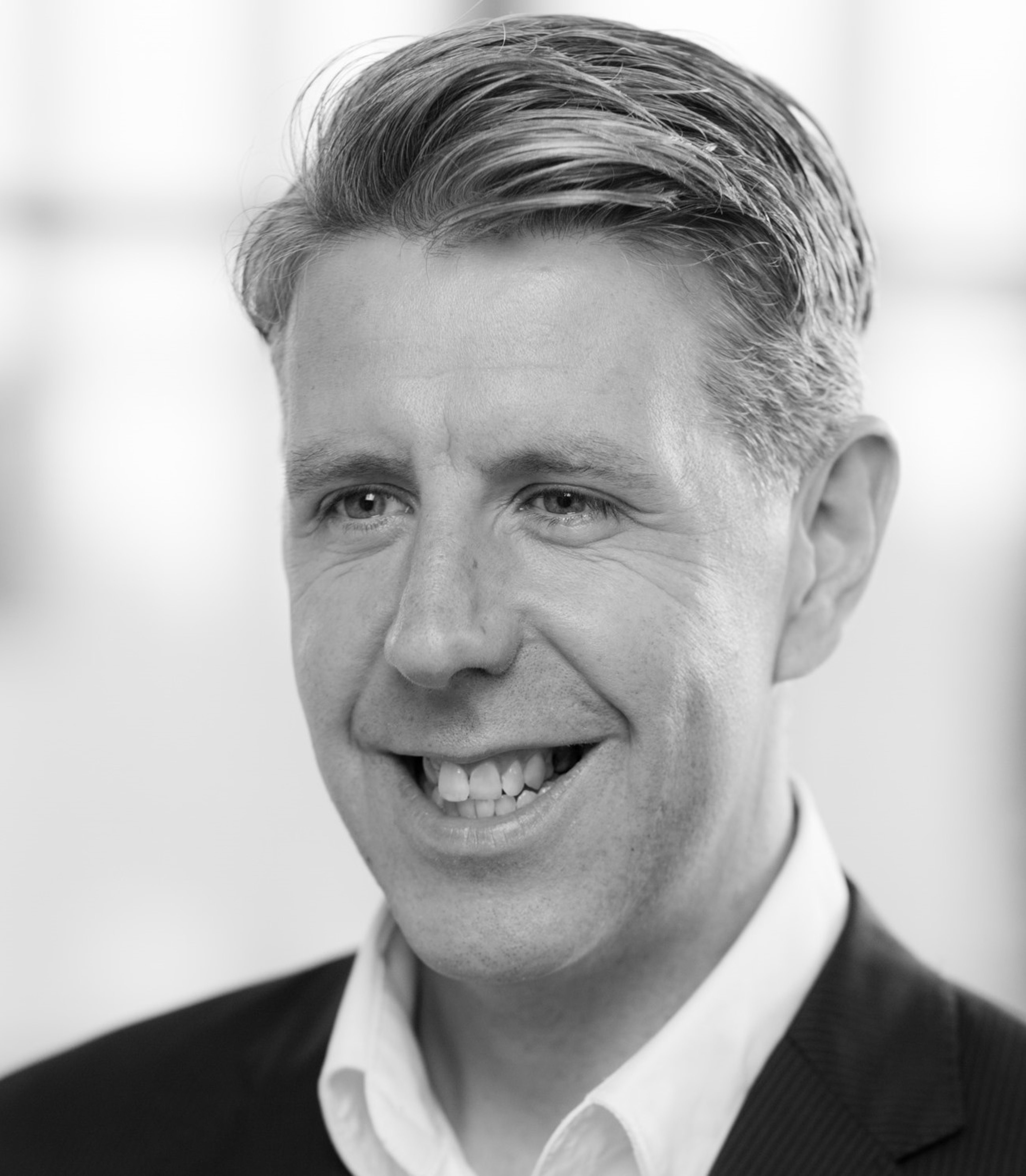 Steven Griffin is shown in a black-and-white image, smiling, wearing a suit jacket and a white shirt. The background appears blurred, focusing on his professional and friendly expression.