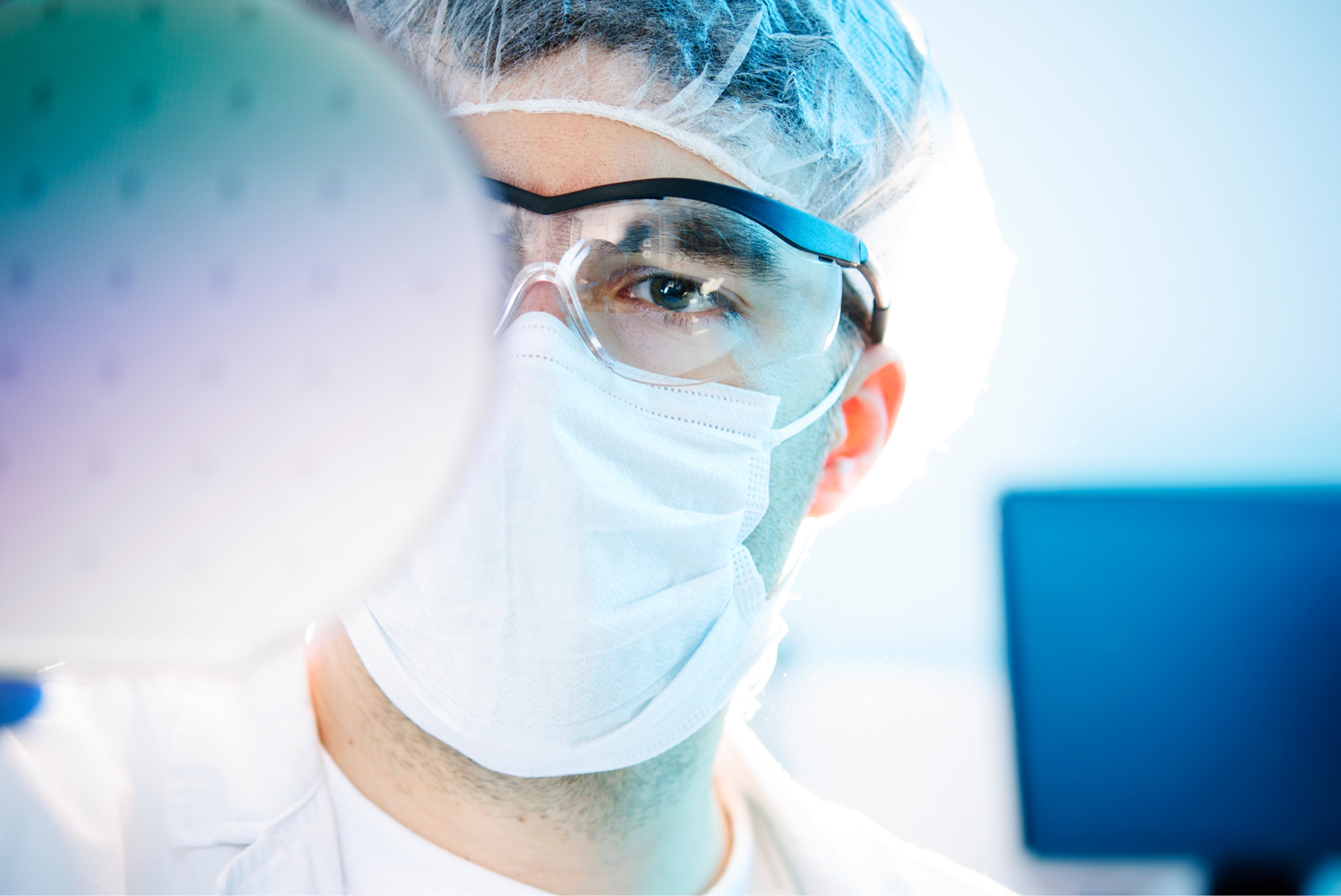 A scientist wearing protective gear examines a silicon wafer in a cleanroom environment.