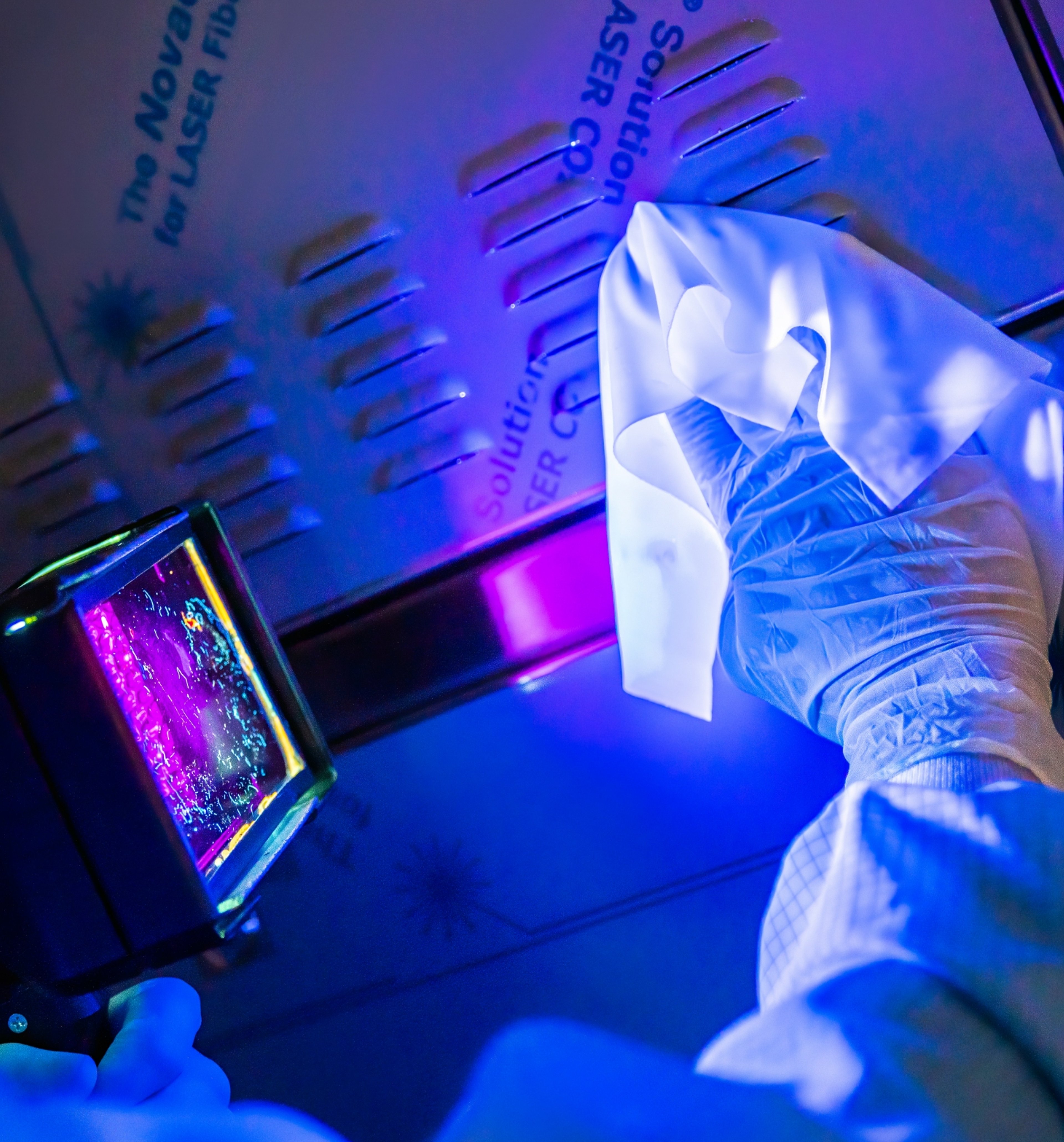 A gloved hand cleans a surface under UV light, revealing contamination, a process used to maintain cleanliness in controlled environments such as pharmaceuticals and electronics.