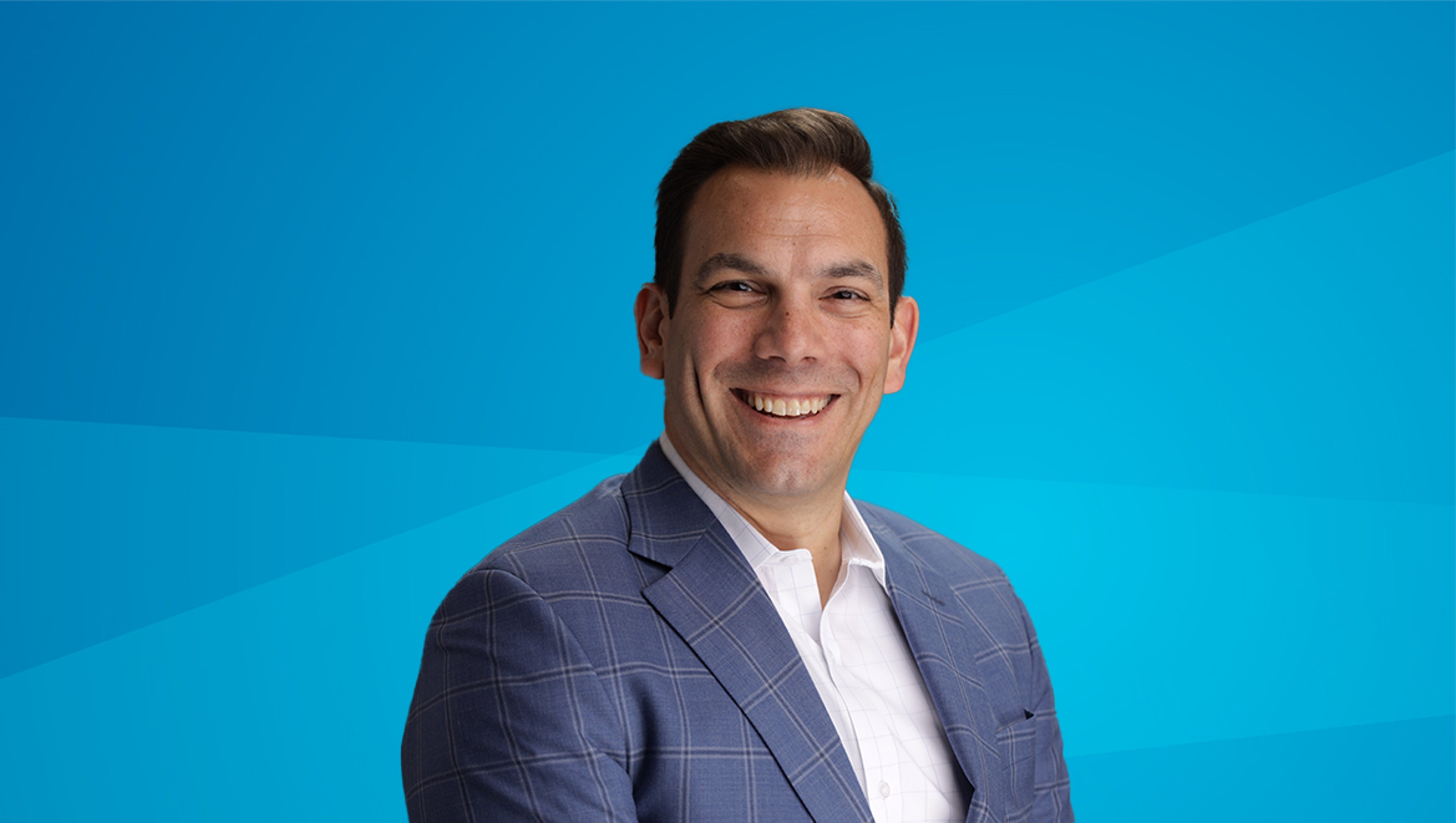 A professional portrait of Chris Albeck, wearing a blue suit and white shirt, smiling confidently against a bright blue background.