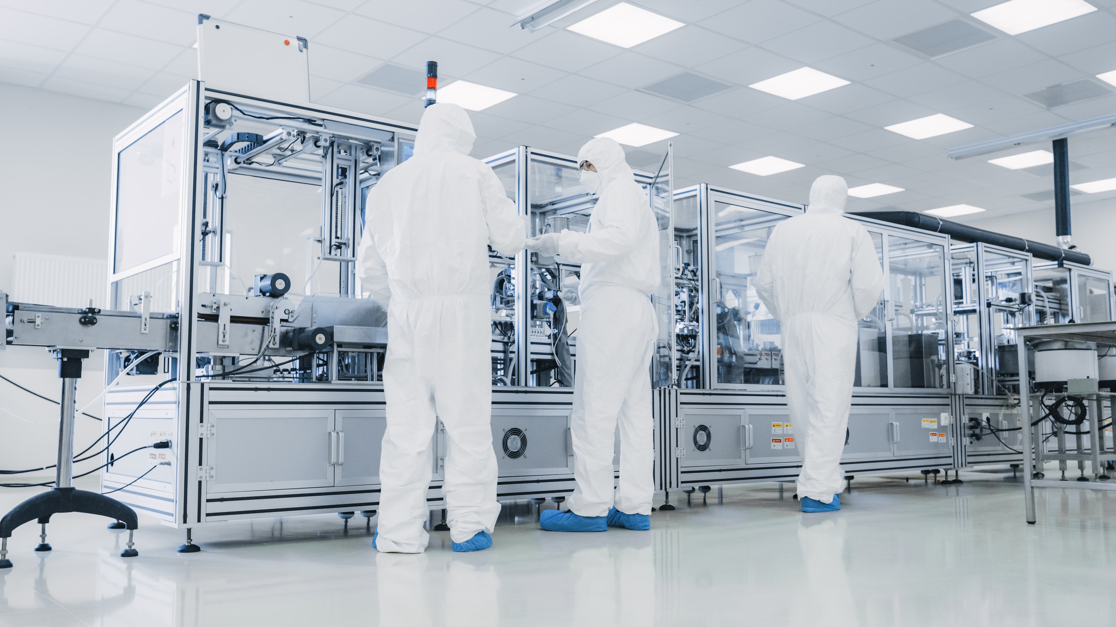 Three persons working on a piece of equipment in a semiconductor manufacturing facility