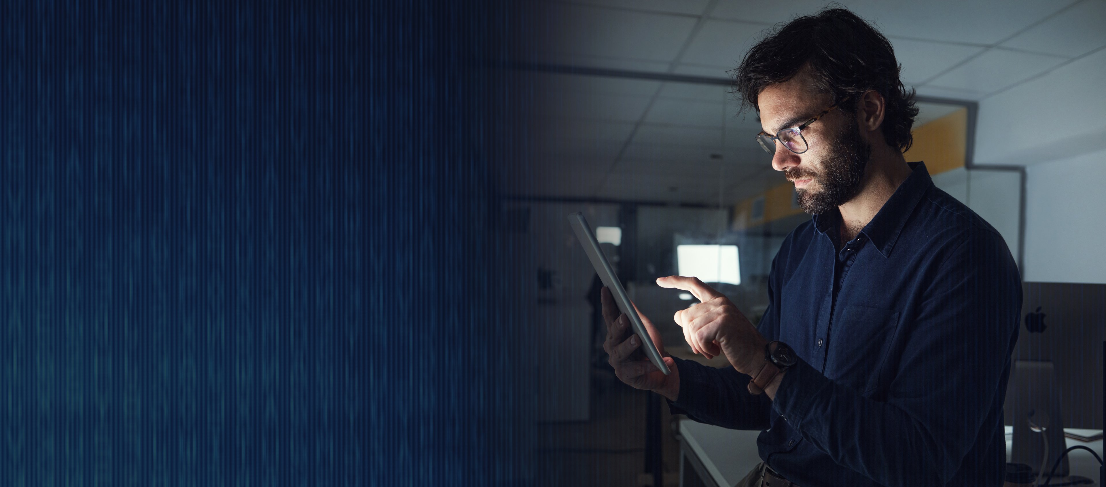 Bearded man in an office looks and clicks on a tablet computer