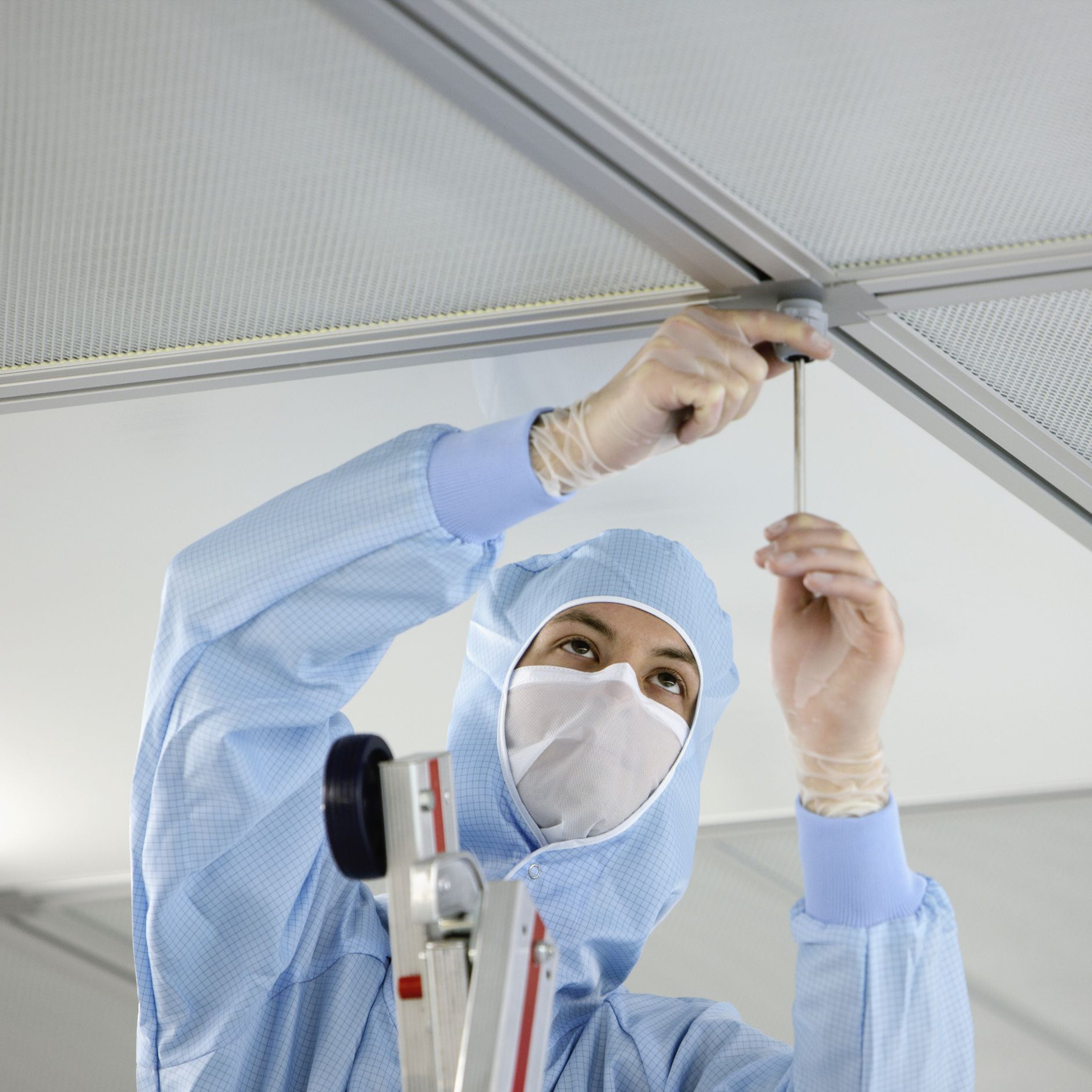 Technician dressed in cleanroom clothes installs a ceiling panel