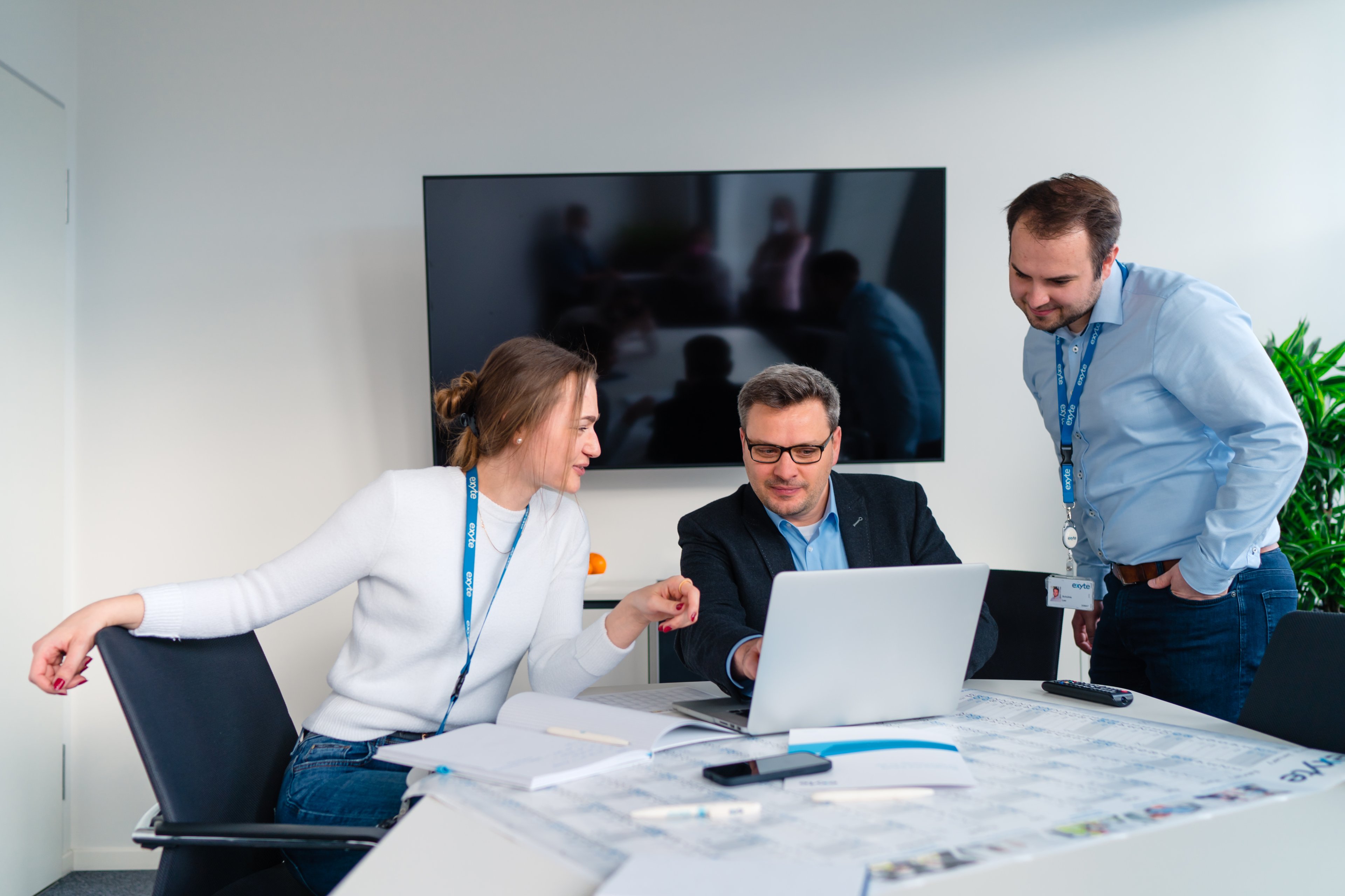 Three Exyte employees in an office showing each other something on a laptop computer