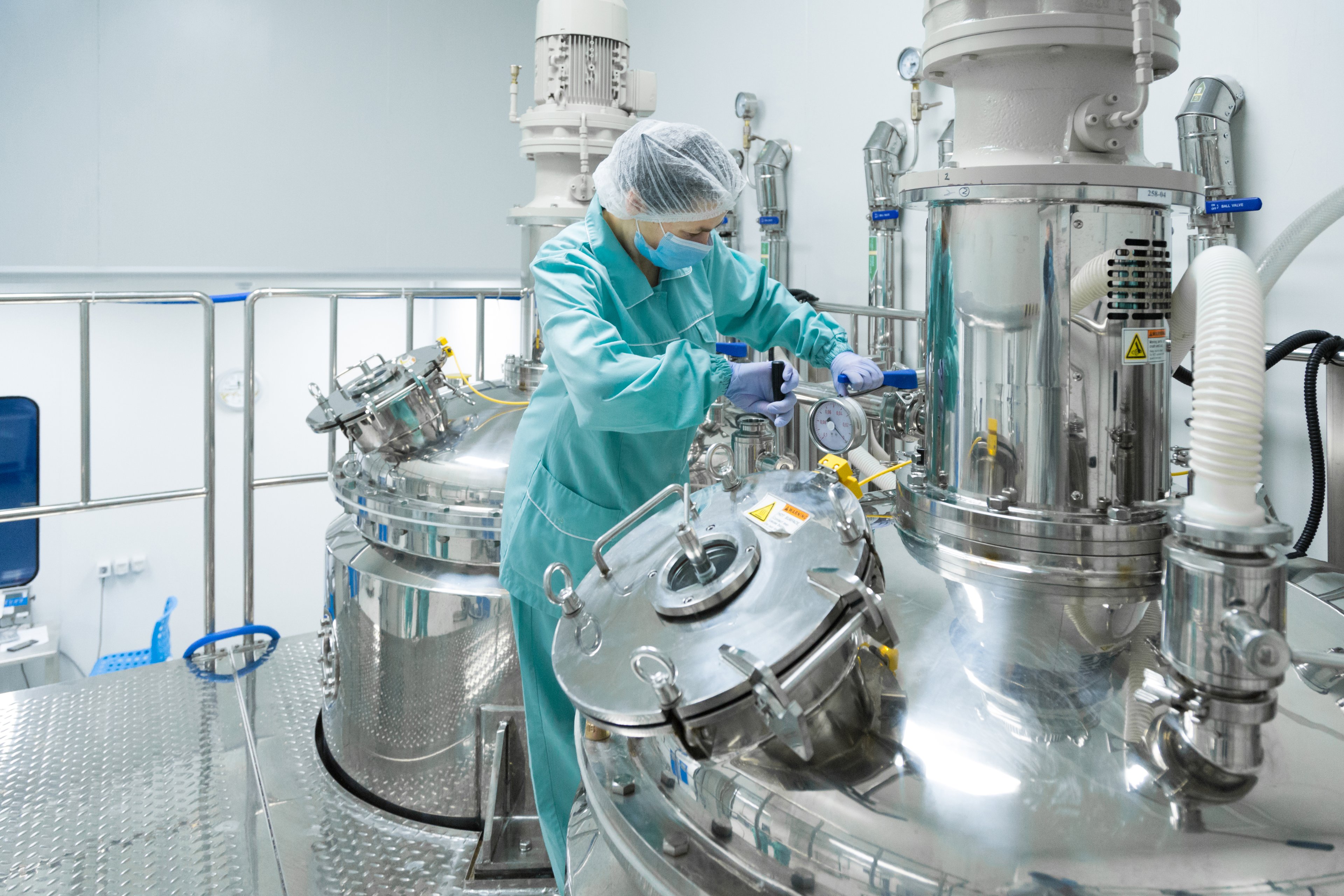 Pharmaceutical factory woman worker in protective clothing operating sterile machinery in a clean production environment.