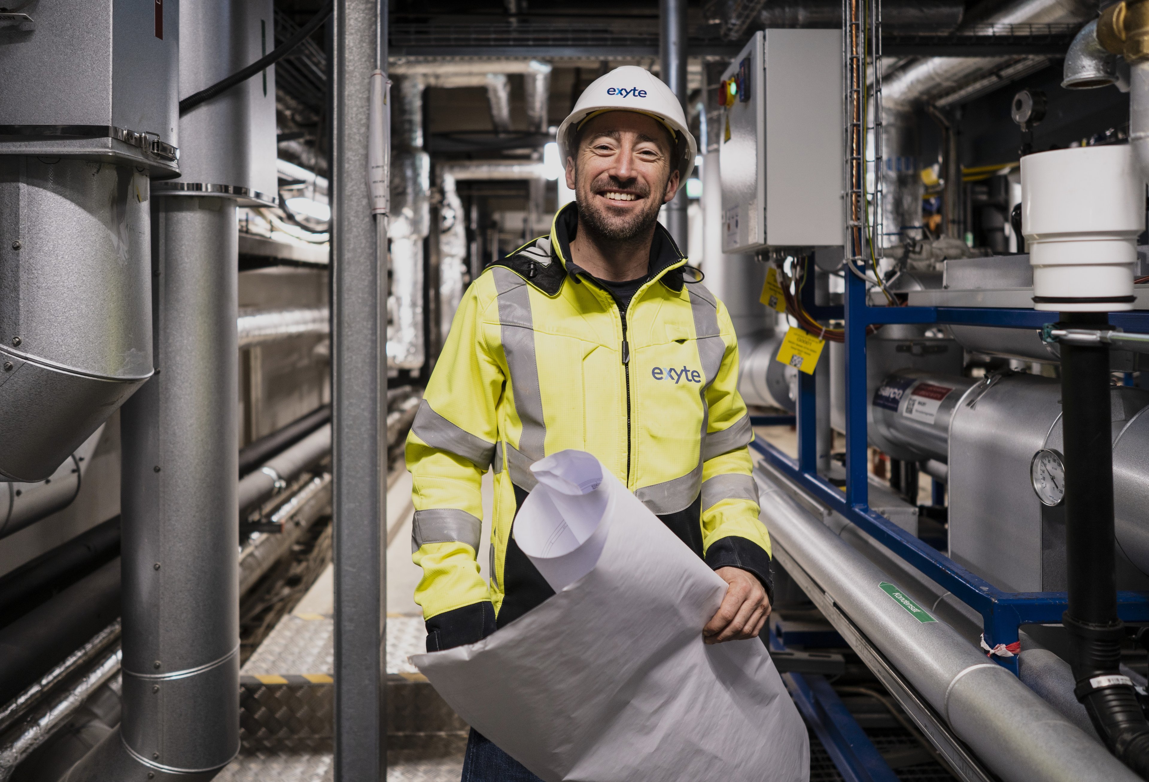 Man with Personal Protective Equipment looks into the camera while holding a construction plan