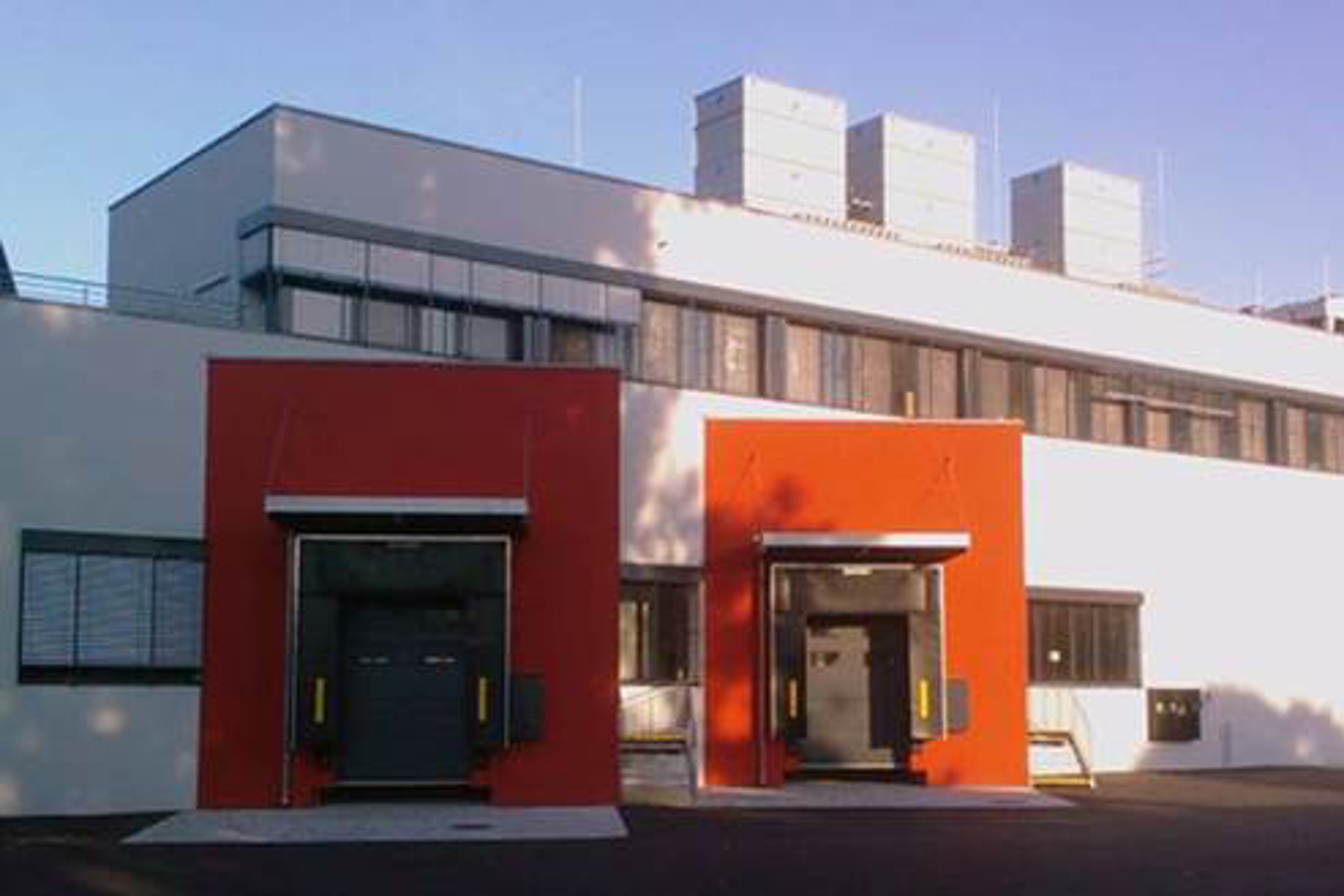 An exterior view of a pharma production facility in Vienna, featuring a modern white building with two red loading docks at the front.
