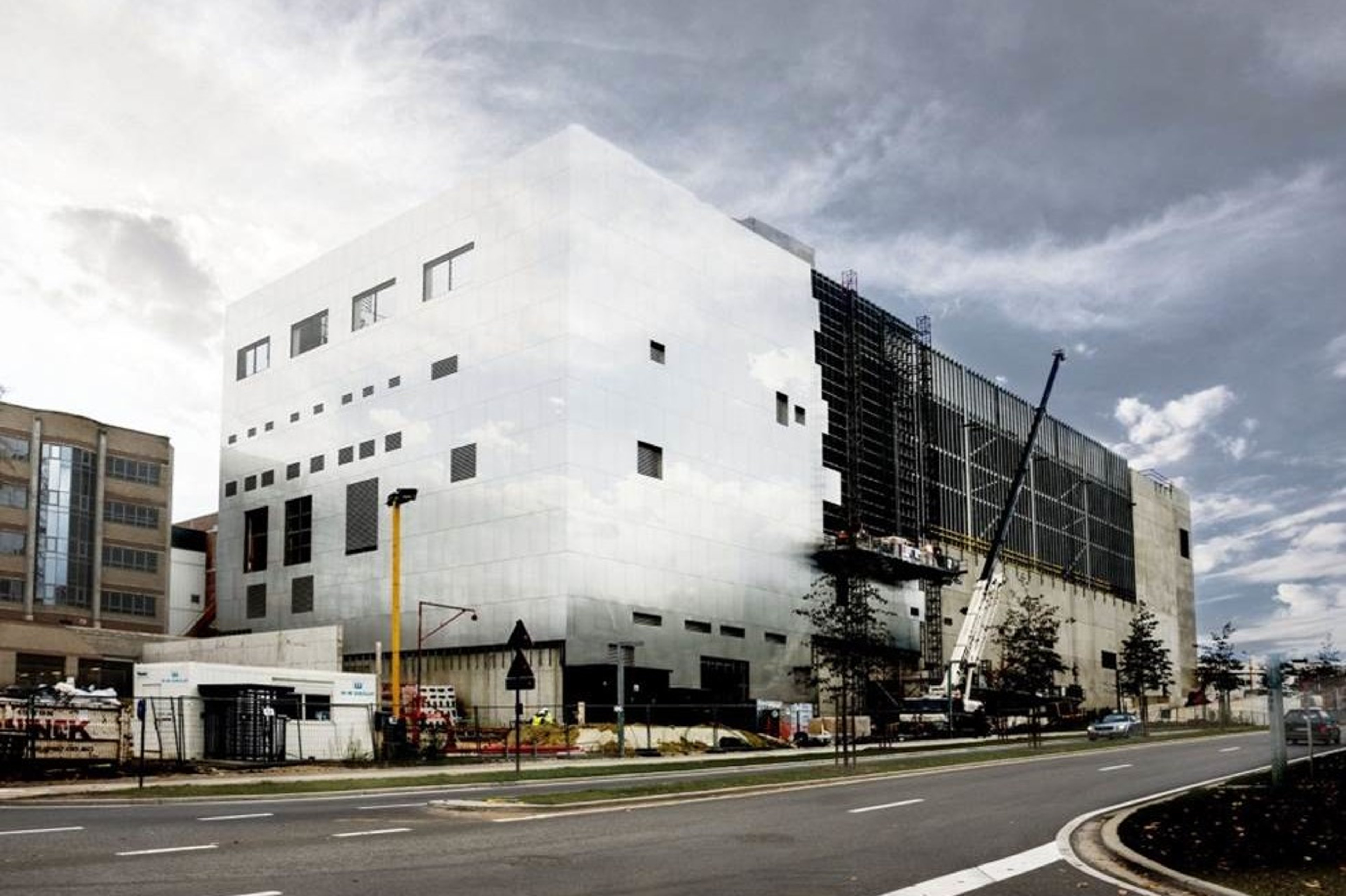 An exterior view of the Nanotech Research Institute in Leuven, featuring a modern, angular building under construction with cranes and scaffolding in place.