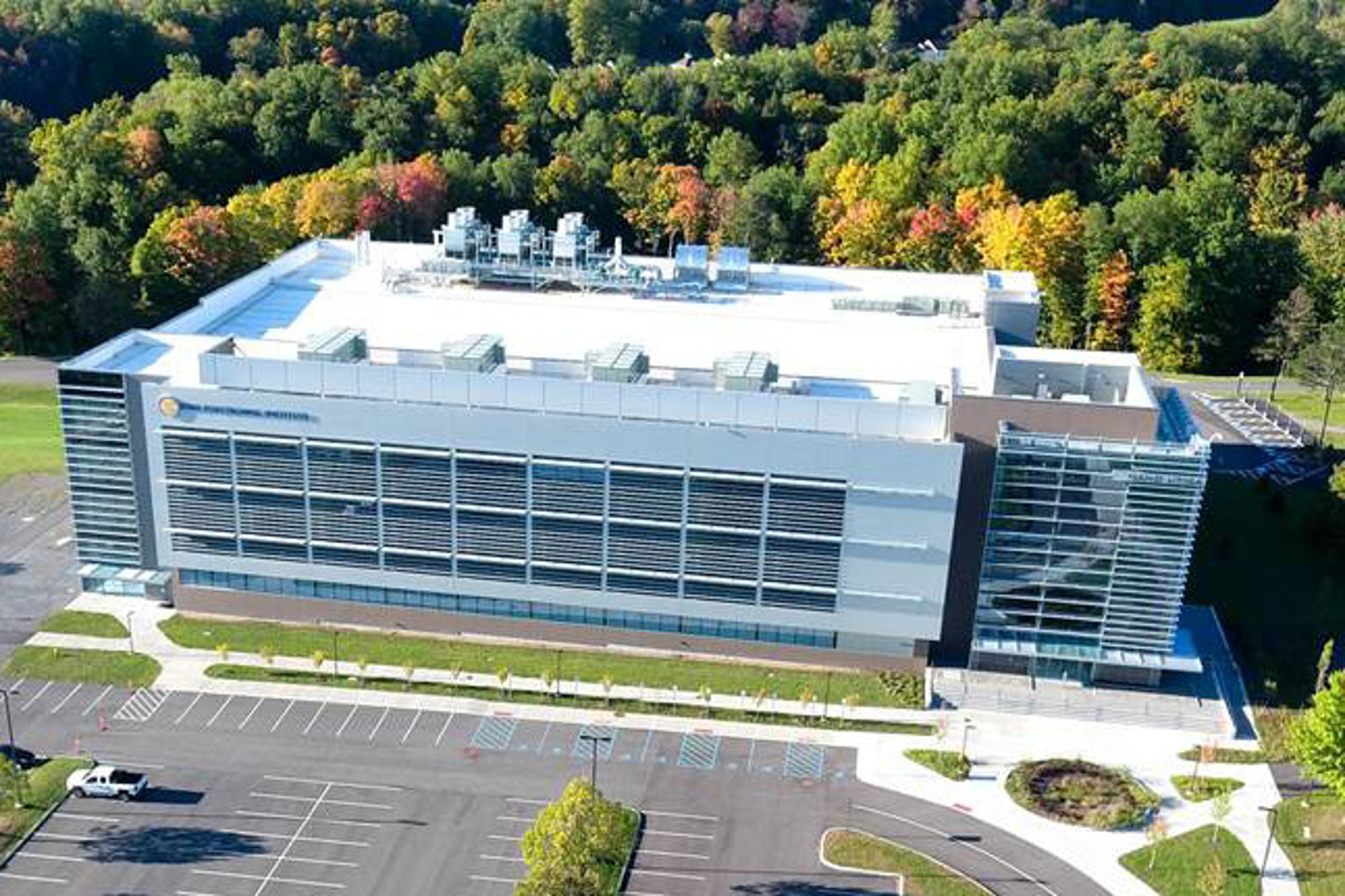 An aerial view of a research building in Utica, NY, surrounded by trees and parking.