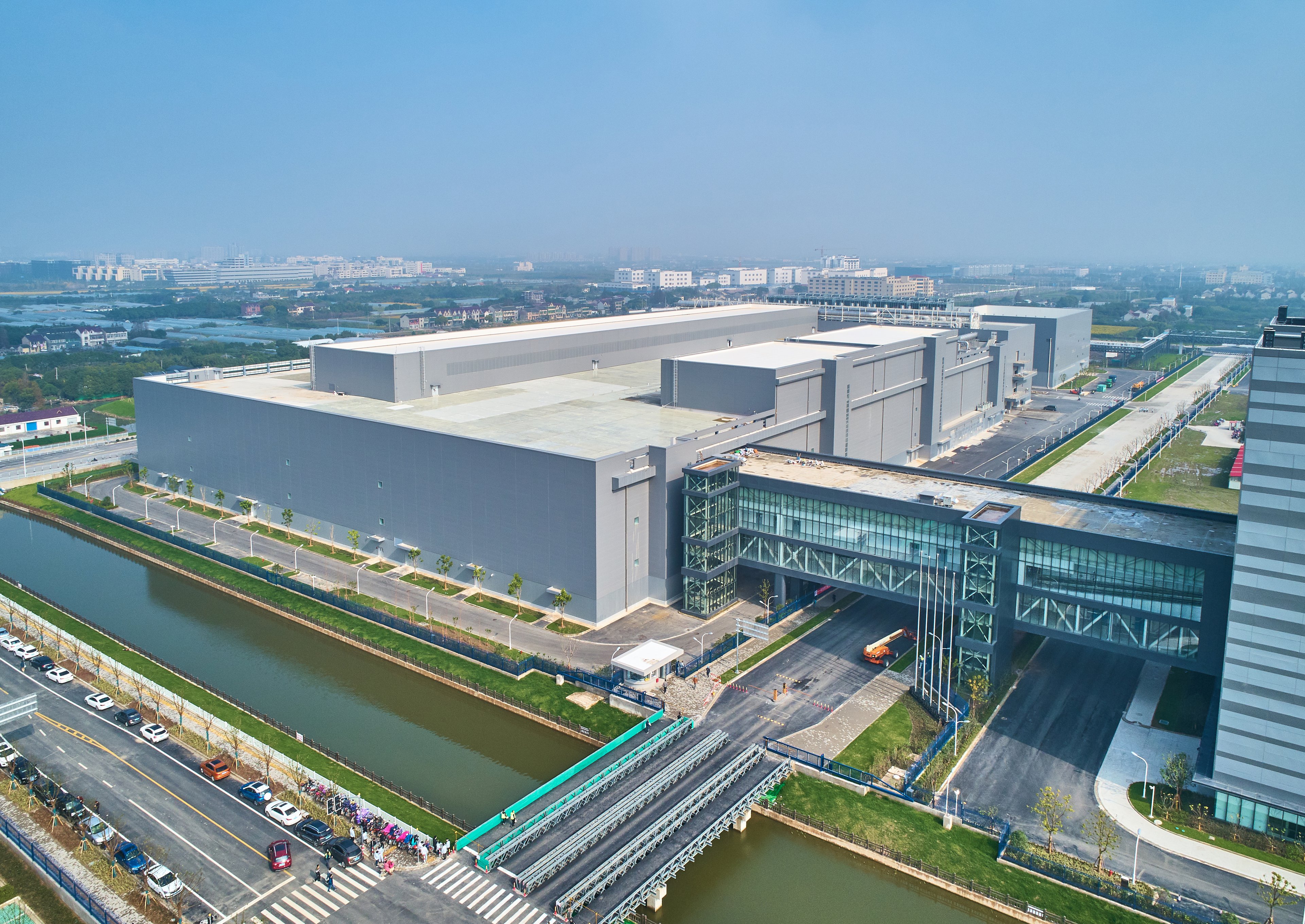 An aerial view of a 300 mm wafer fabrication facility in Shanghai, featuring large industrial buildings, a connecting skybridge, and a surrounding canal.