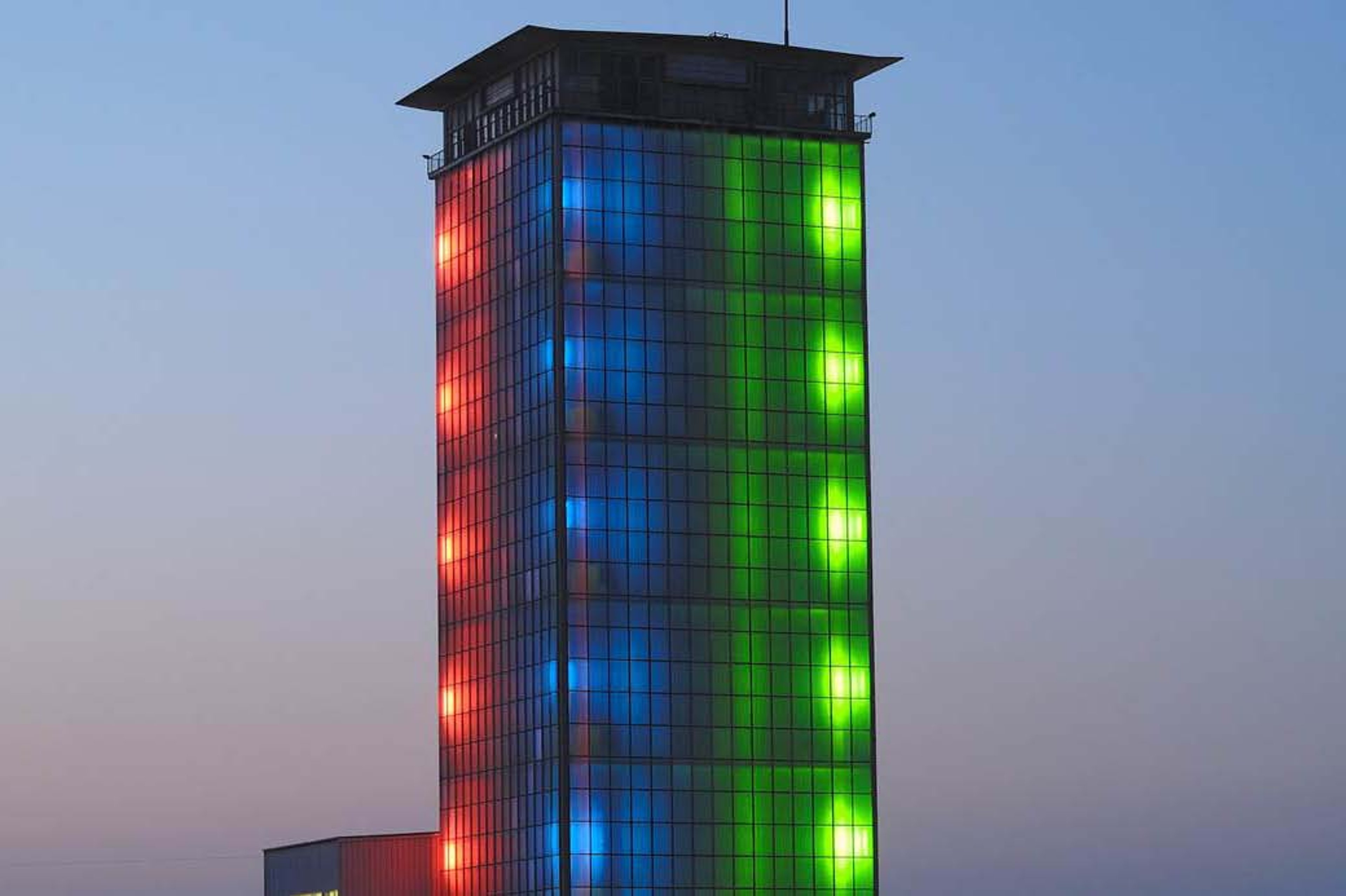 A tall building in Switzerland illuminated with vibrant red, blue, and green lights as part of the Masterplan GMP improvement.