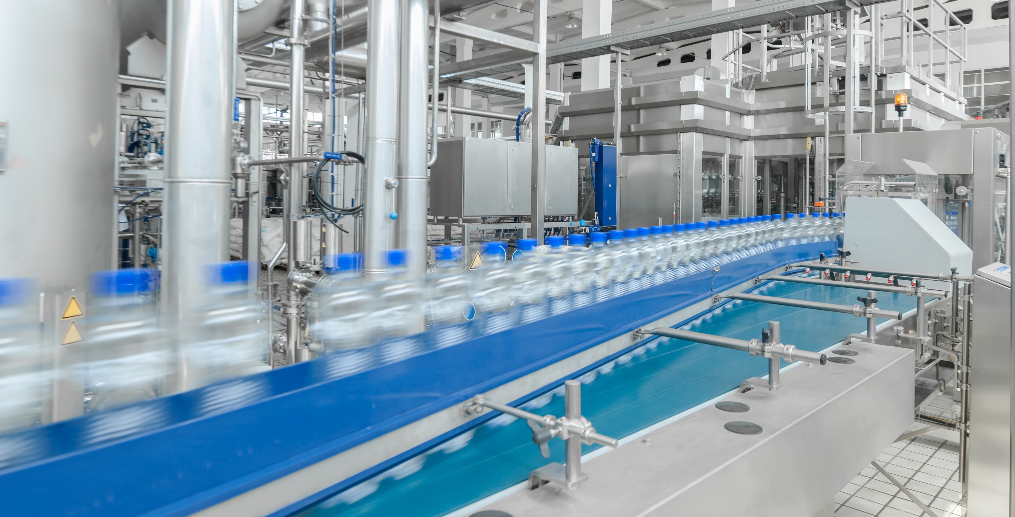 An automated production line for bottling water or similar beverages, showing fast-moving bottles on a conveyor belt in a high-tech facility.