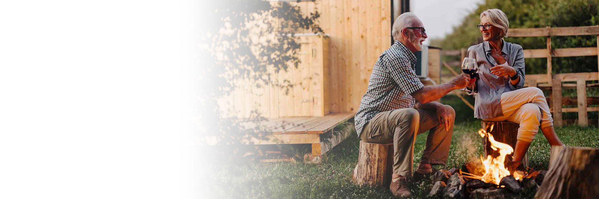 An older couple drinking by a firepit before sunset. 