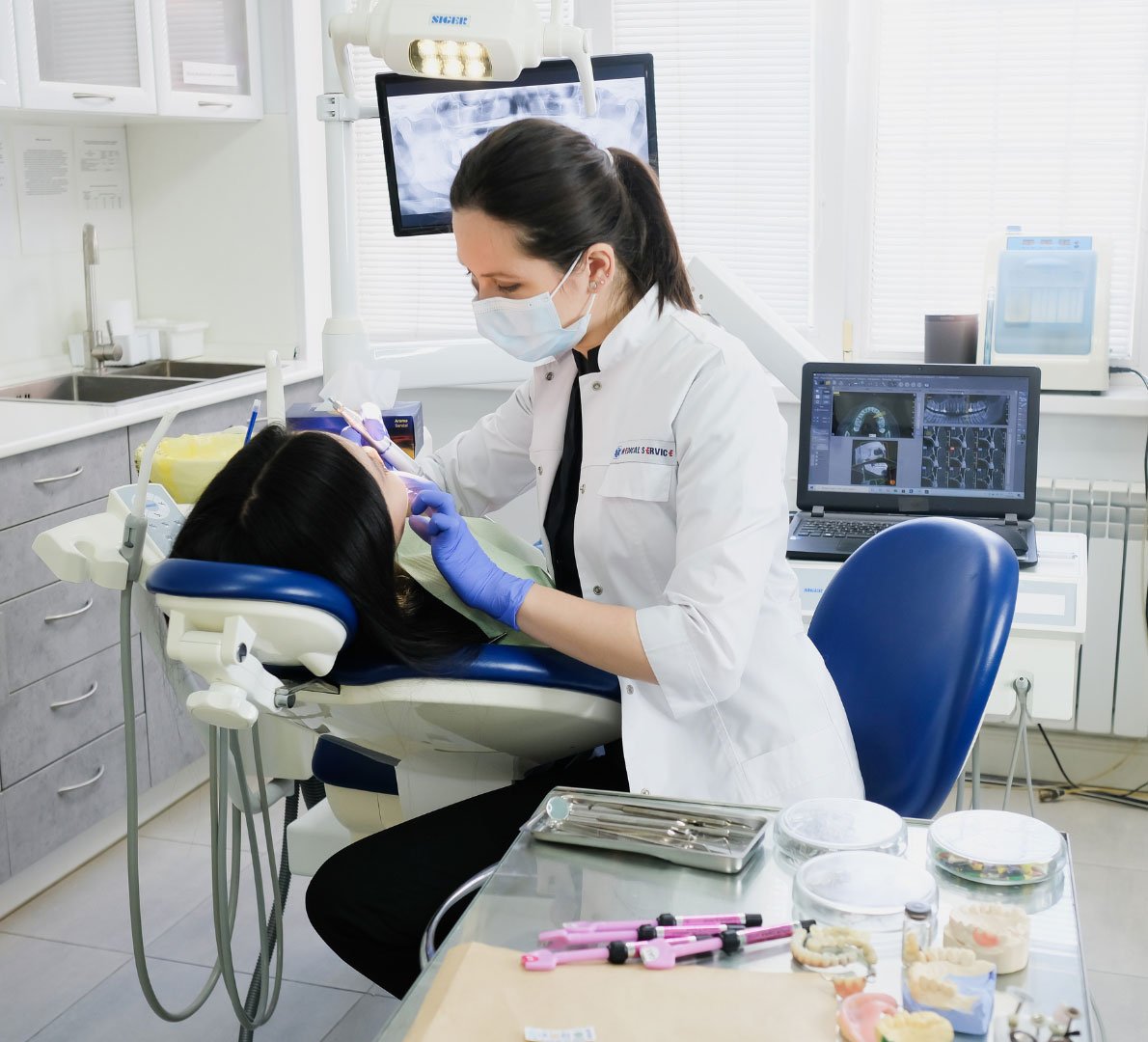 A dental hygienist in a mask providing dental treatment to a female patient in a well-equipped dental office