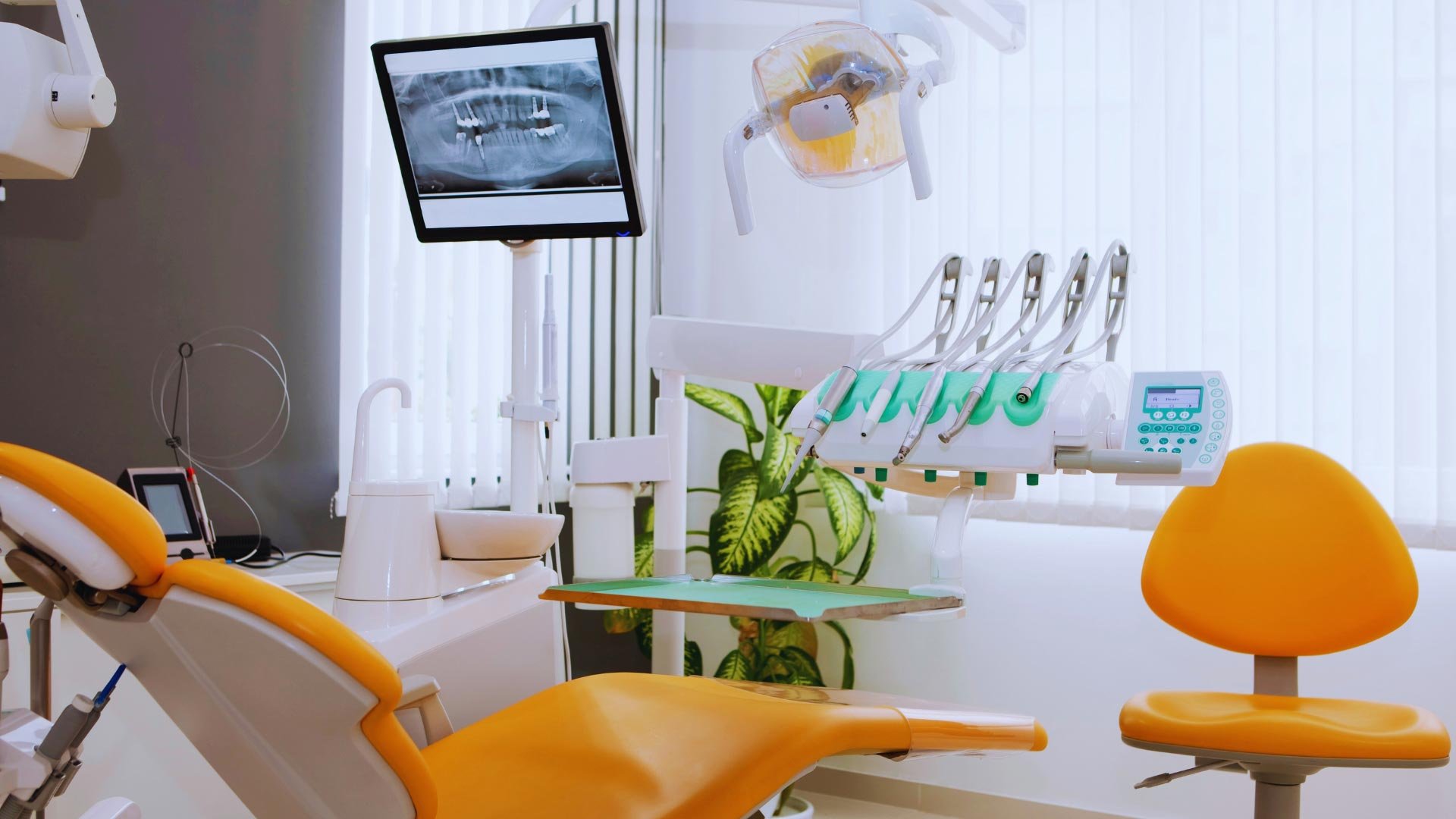 A modern dental clinic equipped with advanced dental technology, including an orange dental chair and digital X-ray display