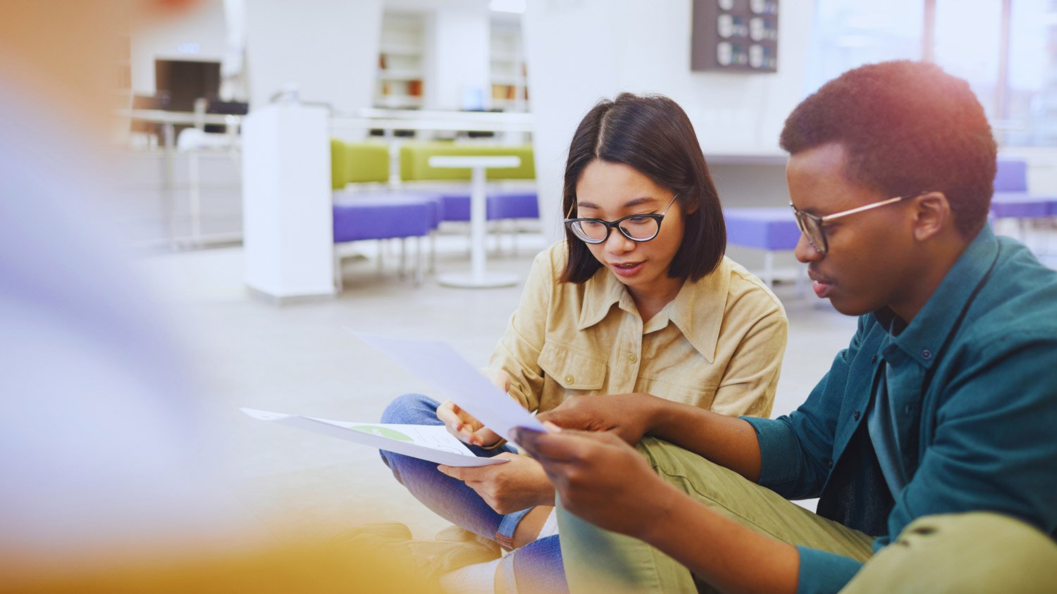 Two young students, a man and a woman, intensely discussing educational materials in a modern study area