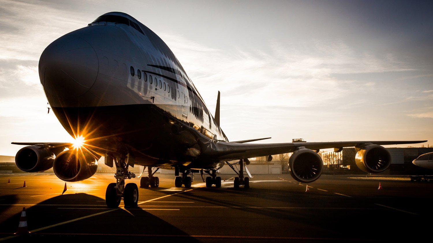 A large airplane at the airport with the sun shining through its engines.
