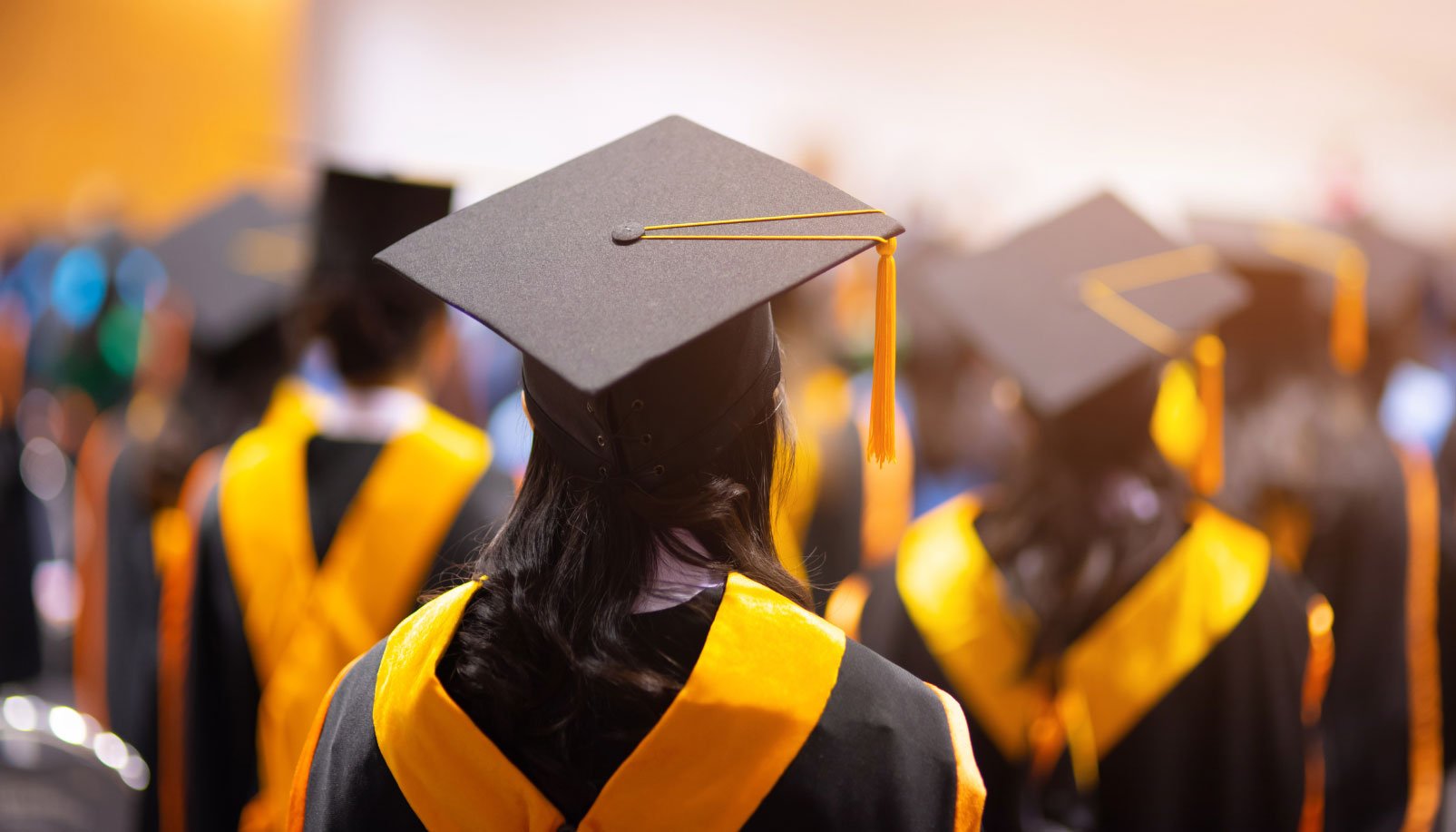 Graduates in black robes with yellow regalia and caps at a university graduation ceremony.