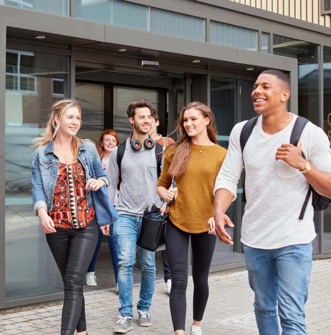 A group of young, diverse students walking happily outside a modern university building, embodying the vibrancy of student life