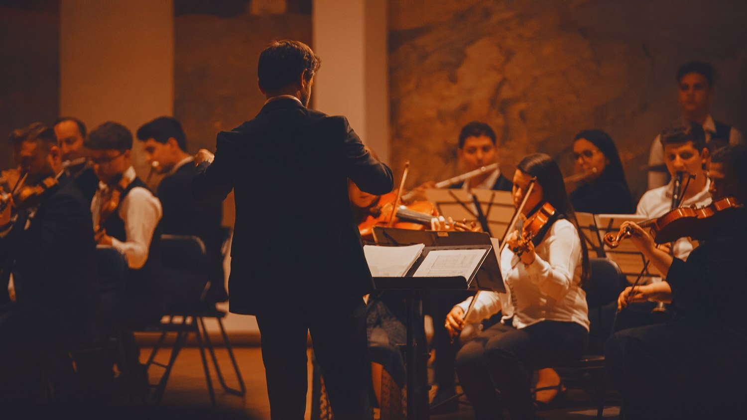 A conductor leading an orchestra, with musicians in formal wear playing string instruments during a concert