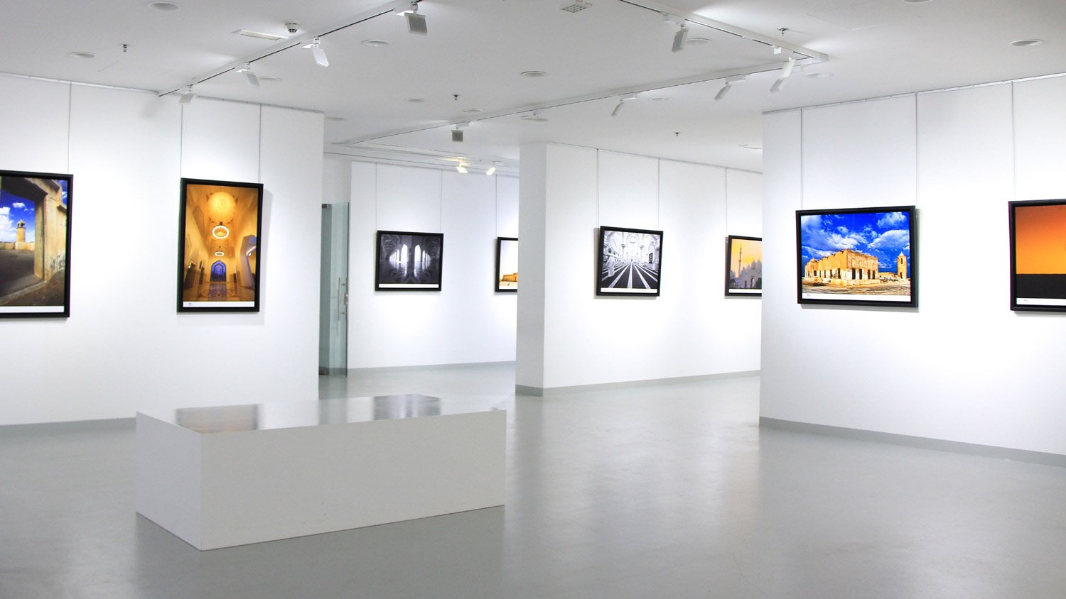 A modern art gallery with various framed photographs of architectural and landscape scenes displayed on white walls
