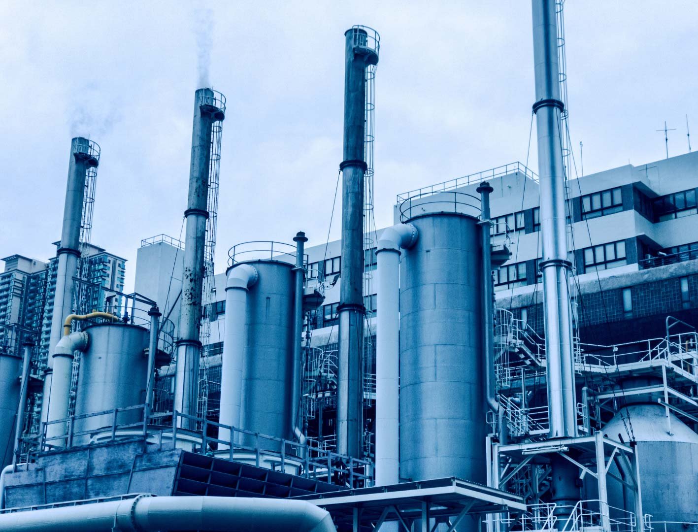 Smokestacks at an industrial plant emitting fumes against a cloudy sky