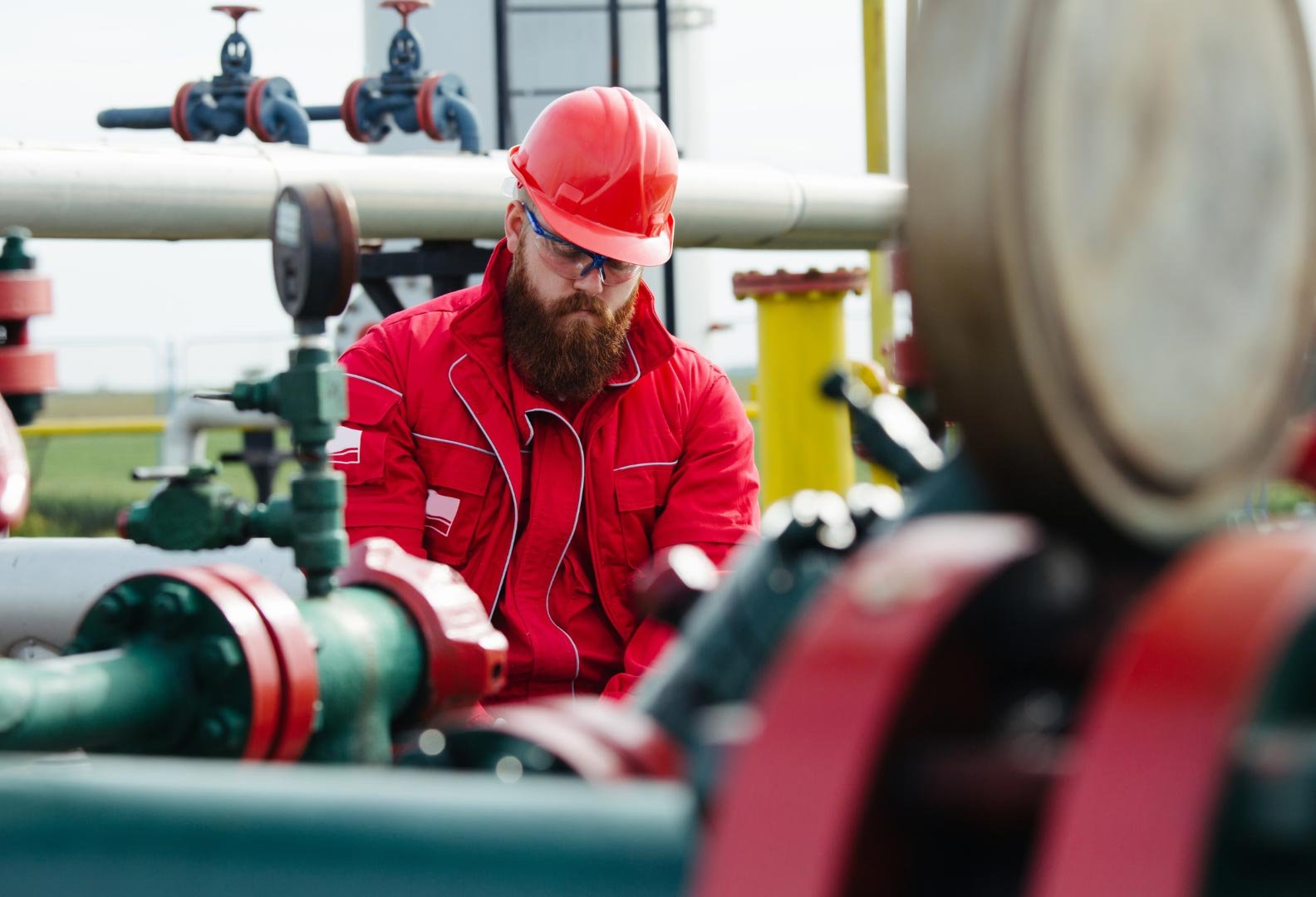 Worker in red overalls inspecting equipment at an oil and gas pipeline facility