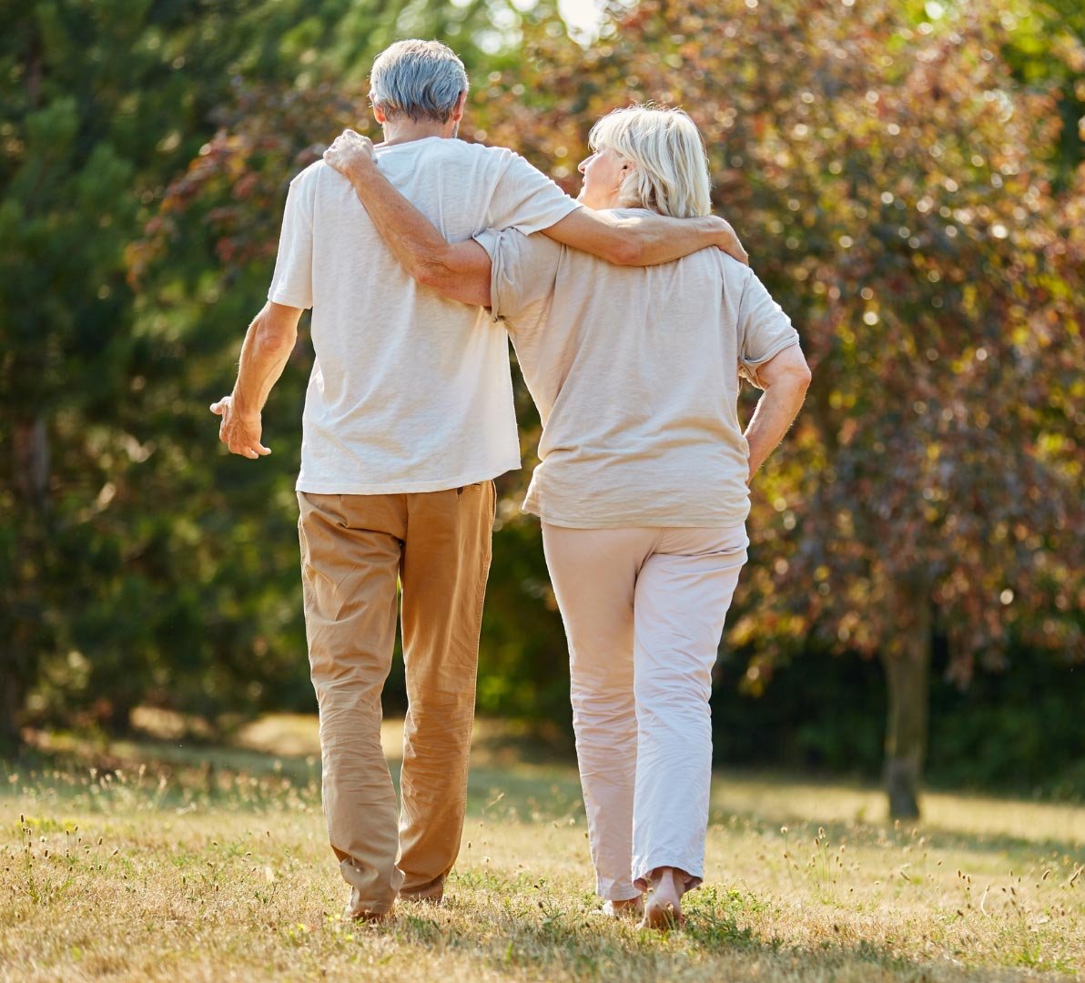An elderly couple walking arm in arm in a sunlit park
