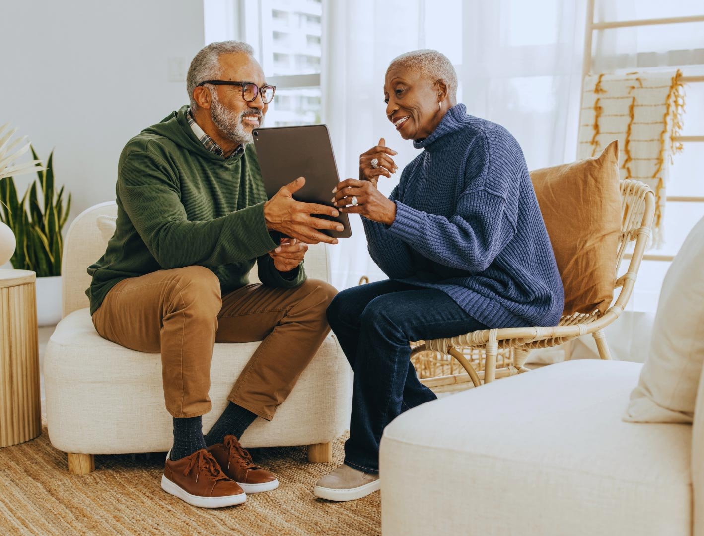 Two senior men, one using a tablet, sharing a laugh together in a living room