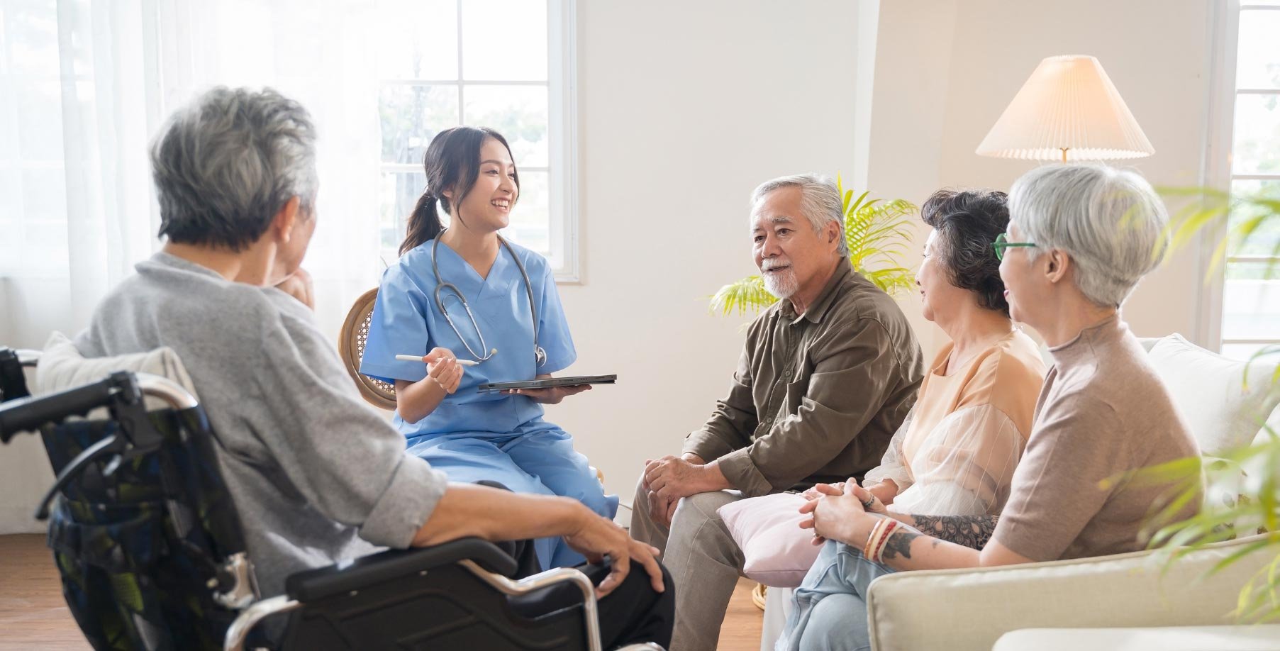 A diverse group of seniors in a bright room listening attentively to a young female nurse