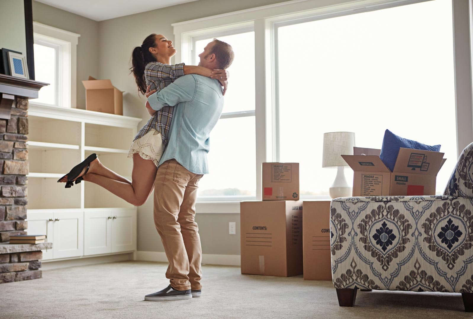 A man lifting a woman in celebration in a new home filled with moving boxes and furniture