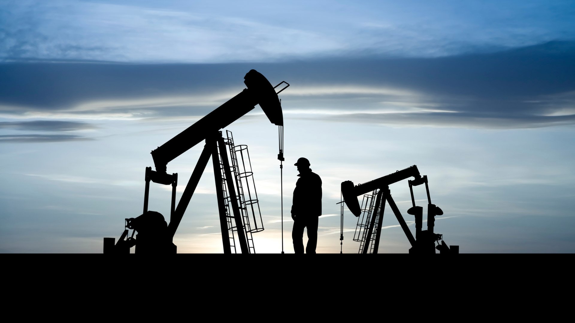 Silhouette of an oil pumpjack and a worker at sunset, symbolizing energy production.
