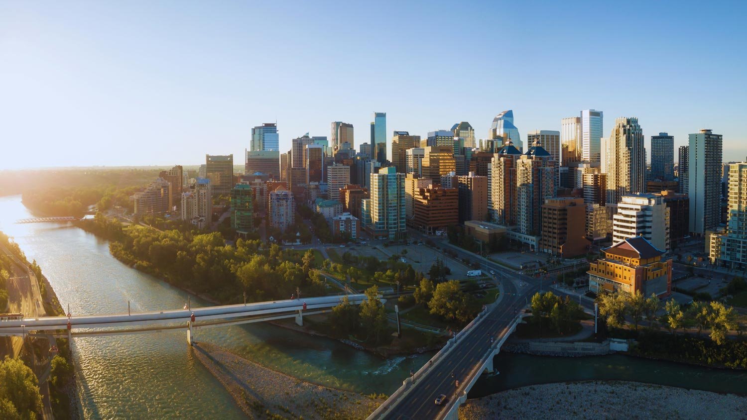 A panoramic view of the Calgary skyline at sunset, showing rivers and bridges.