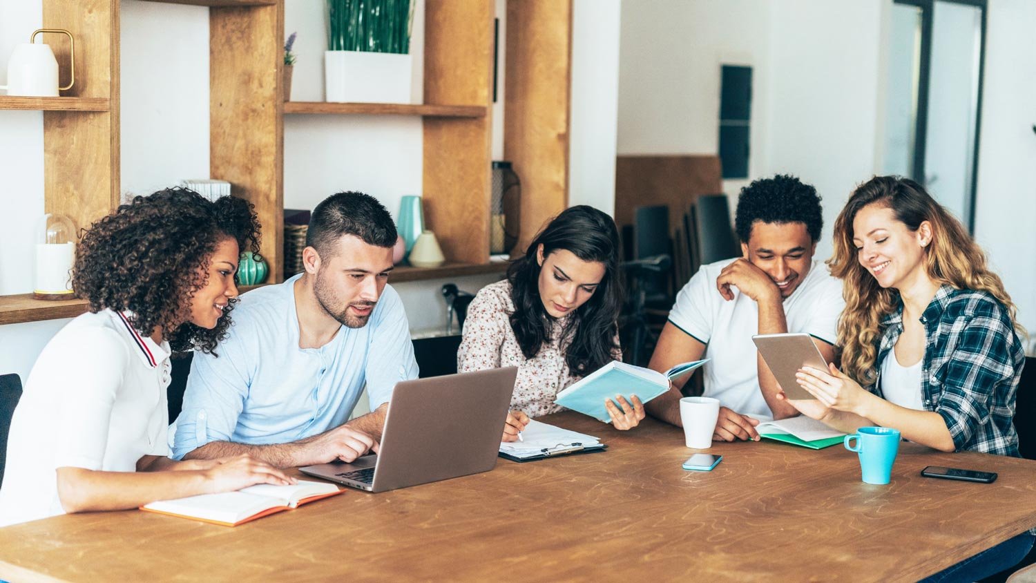 A diverse group of students engaging in a discussion around a laptop in a casual setting.