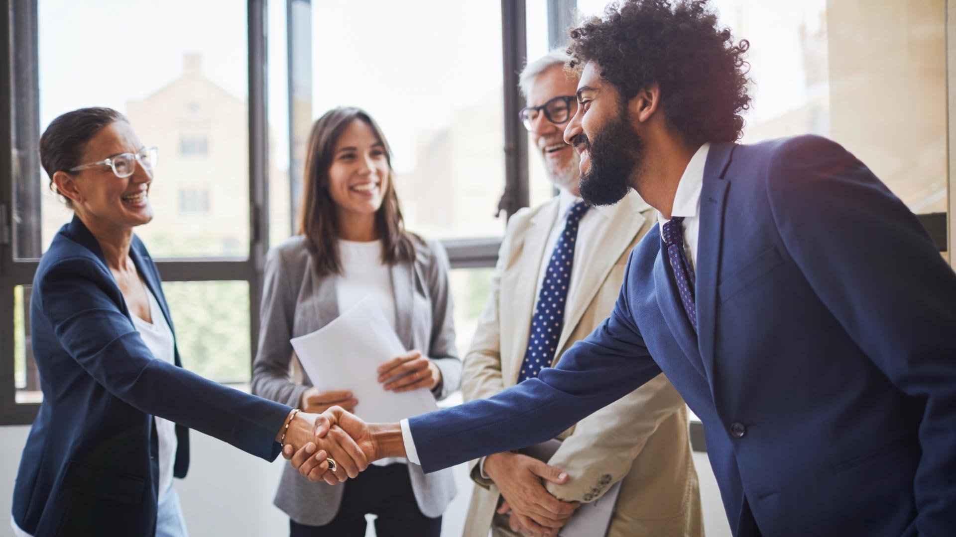 Business professionals shaking hands in a light-filled office, symbolizing agreement or introduction.