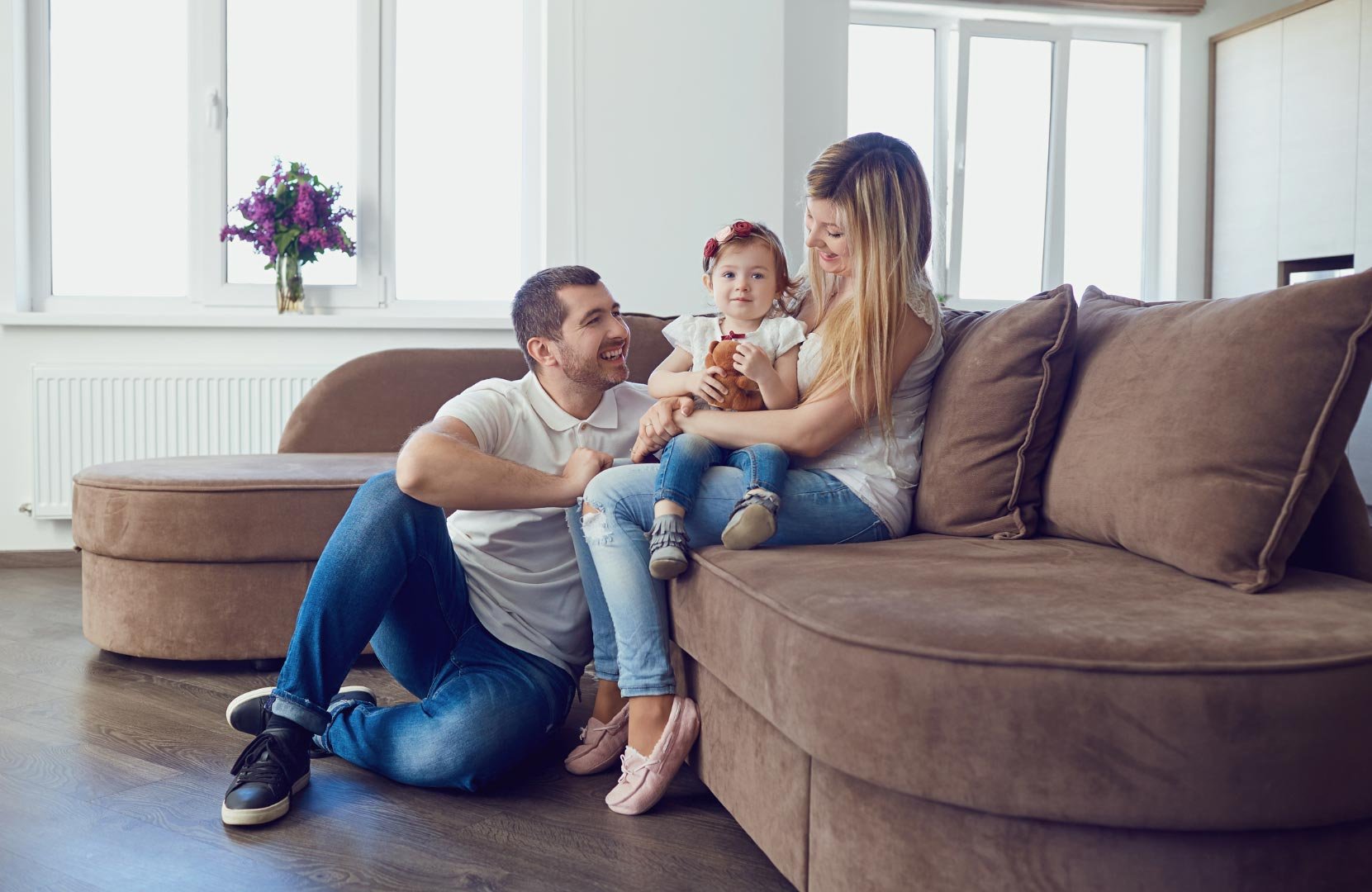 A relaxed family of three, with a toddler, enjoying a moment together on a comfortable living room sofa.
