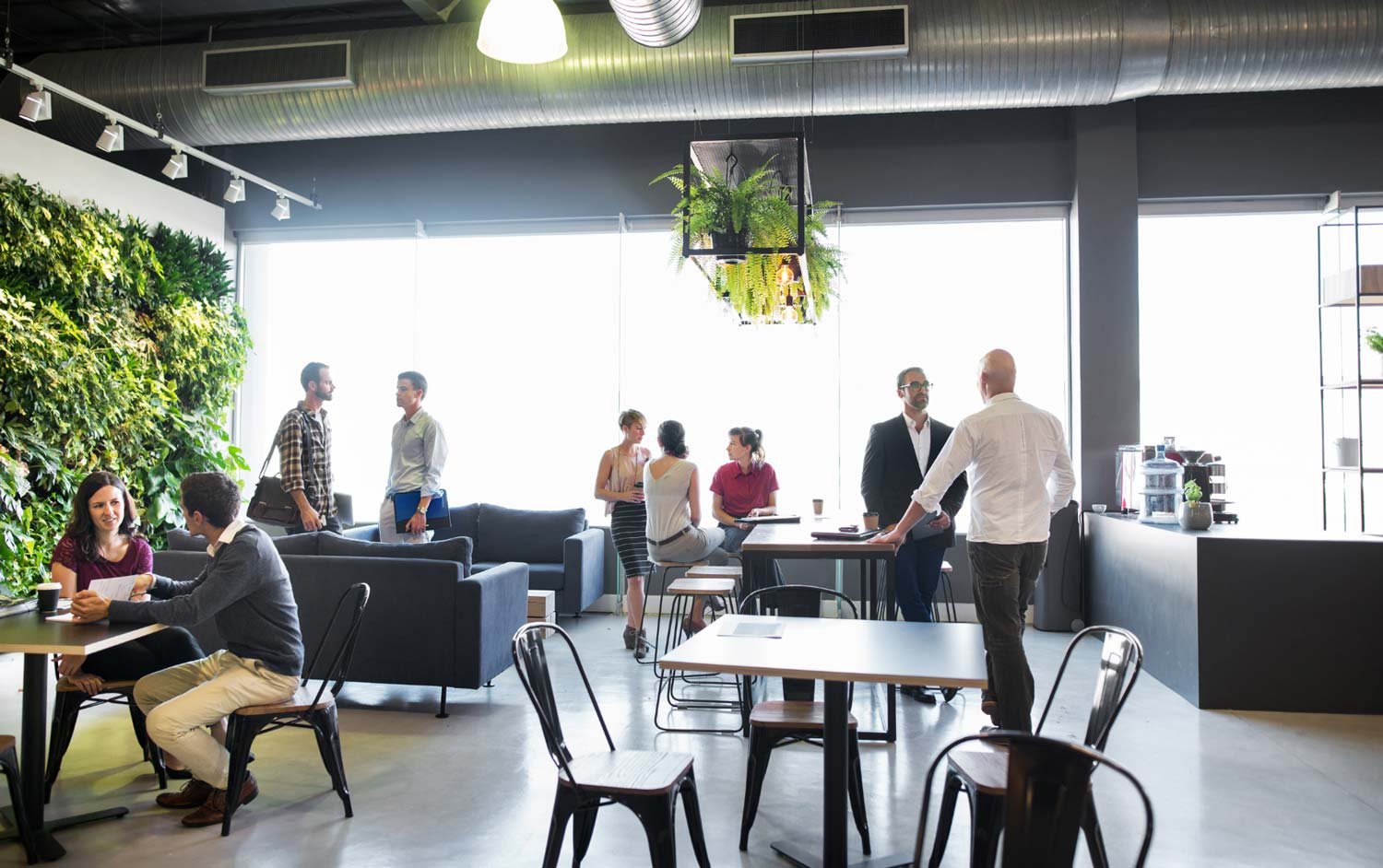 A bustling office space with various groups of professionals engaging in discussions and casual meetings.