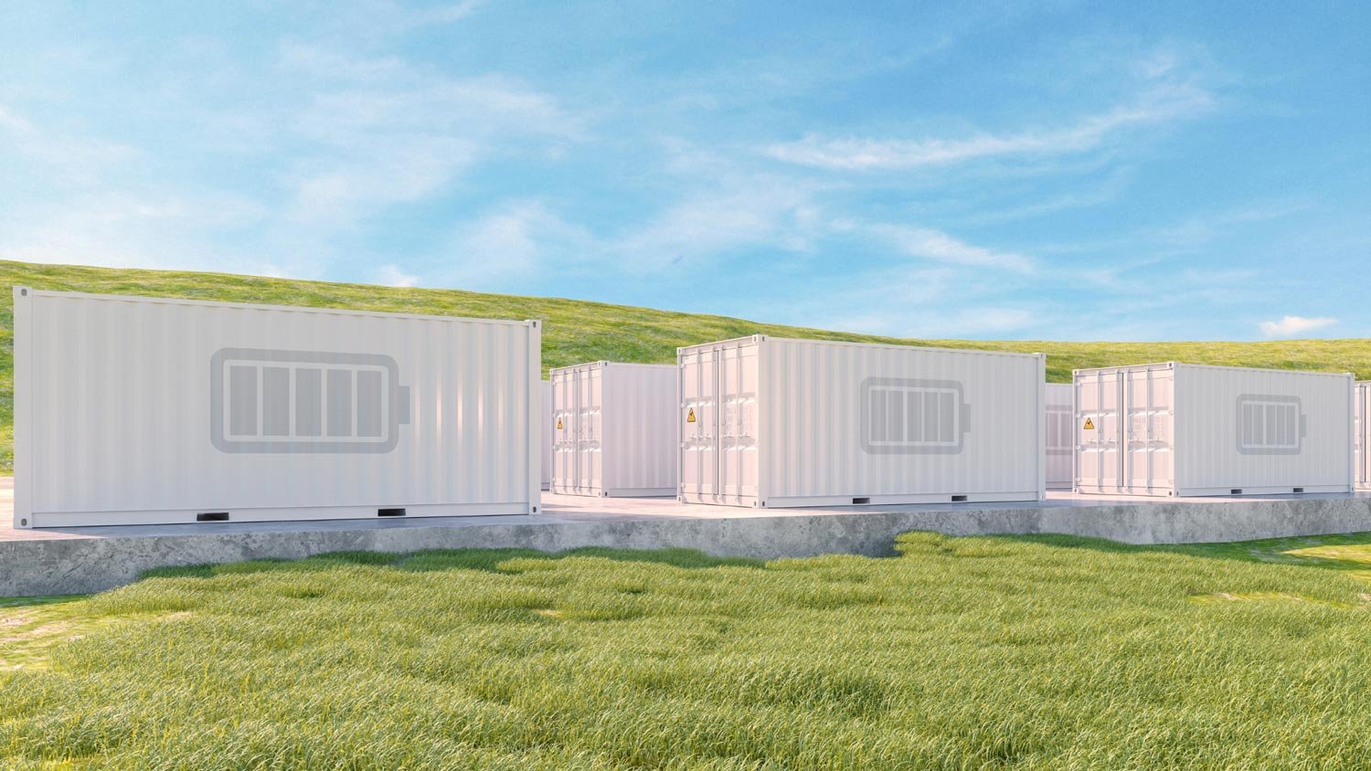 Row of white battery storage containers on green grass under a clear blue sky, representing clean energy storage solutions.