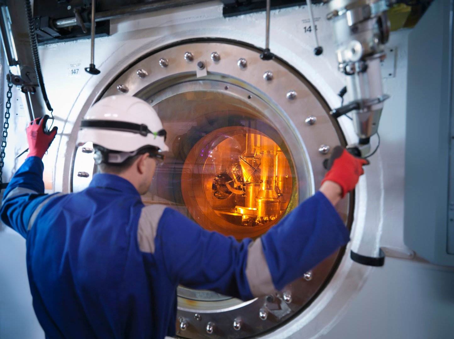 A technician examining complex nuclear machinery through a heavy-duty observation window