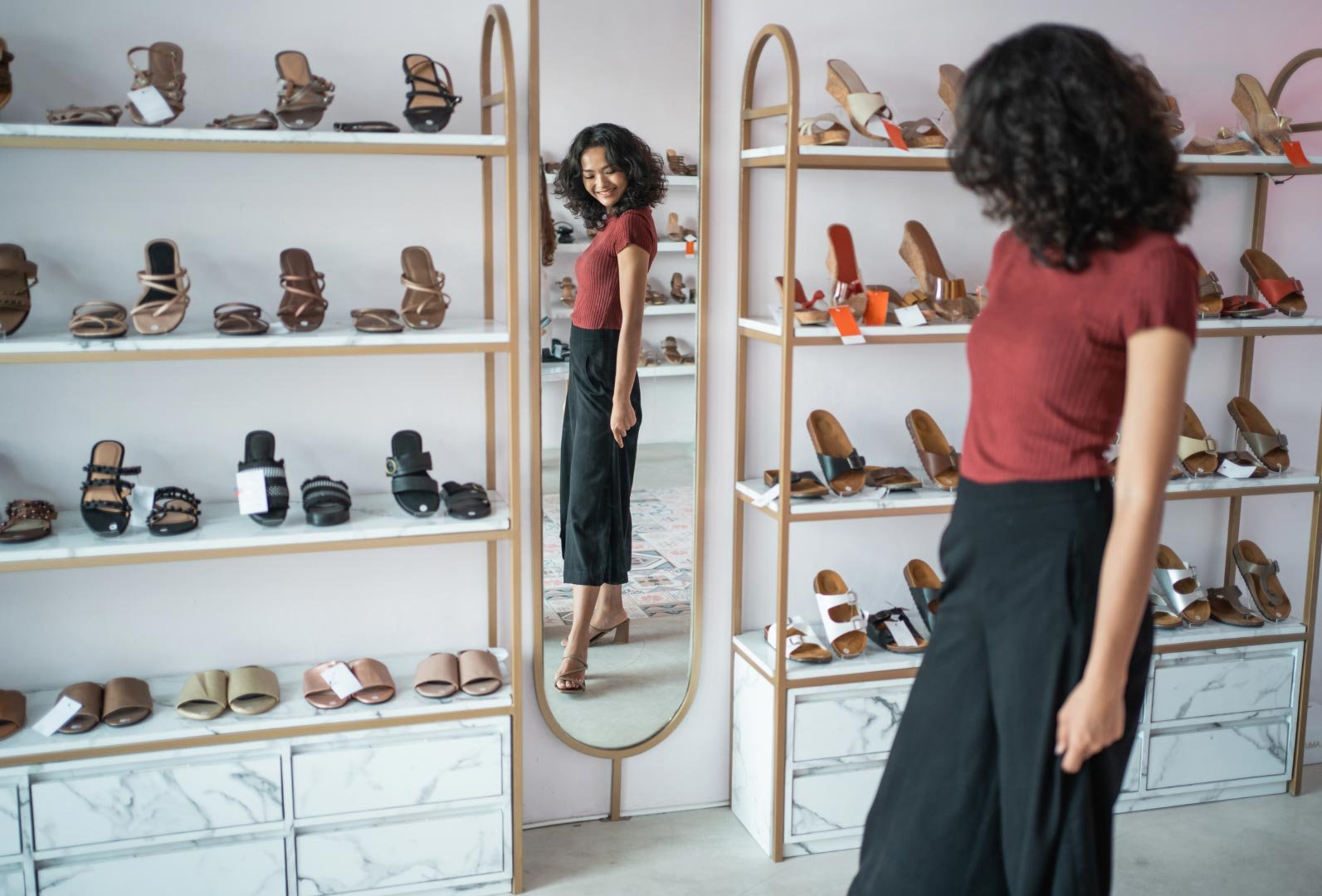 A woman admiring shoes in a modern store with mirrors and white shelves filled with shoes