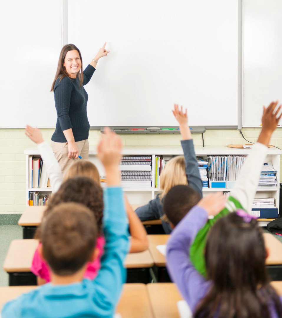 A male teacher points to a digital globe on a screen in front of attentive students