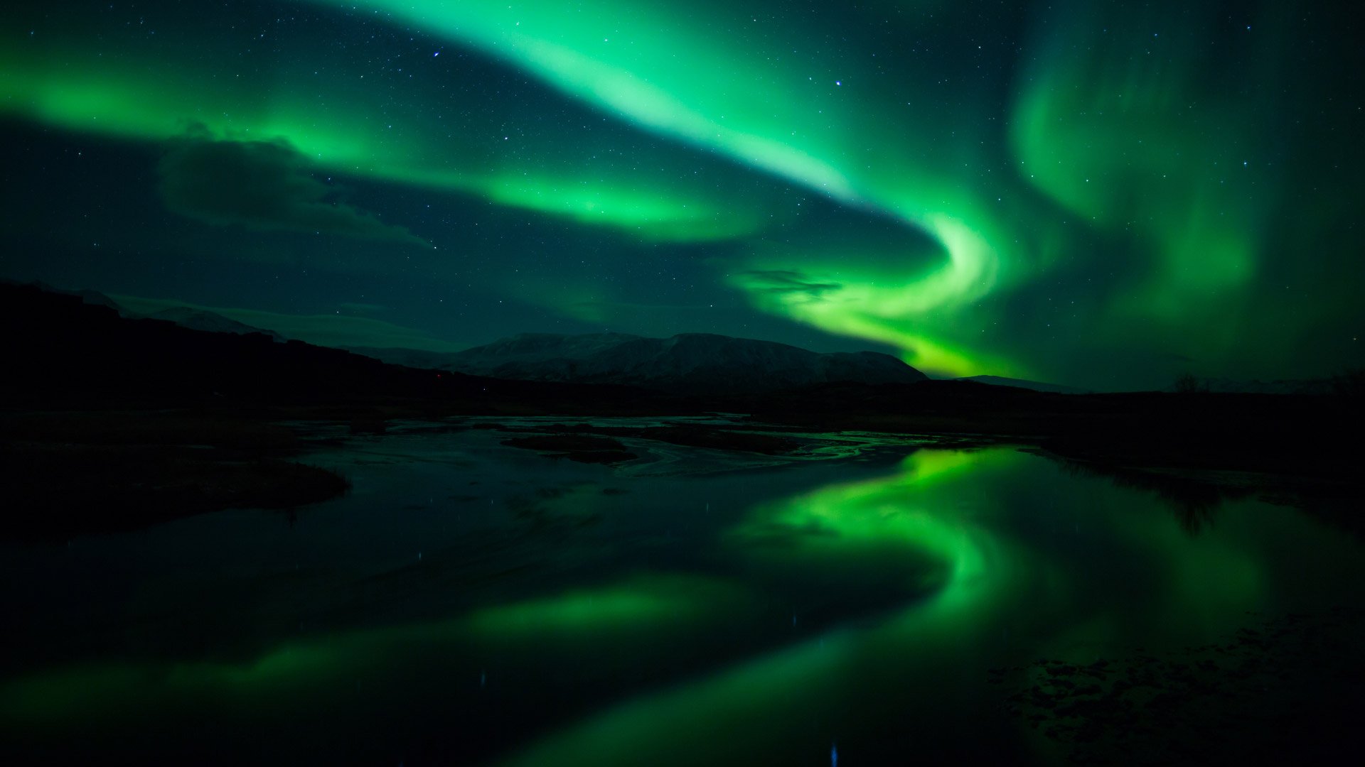 Vibrant green aurora borealis swirling in the night sky above a reflective water surface